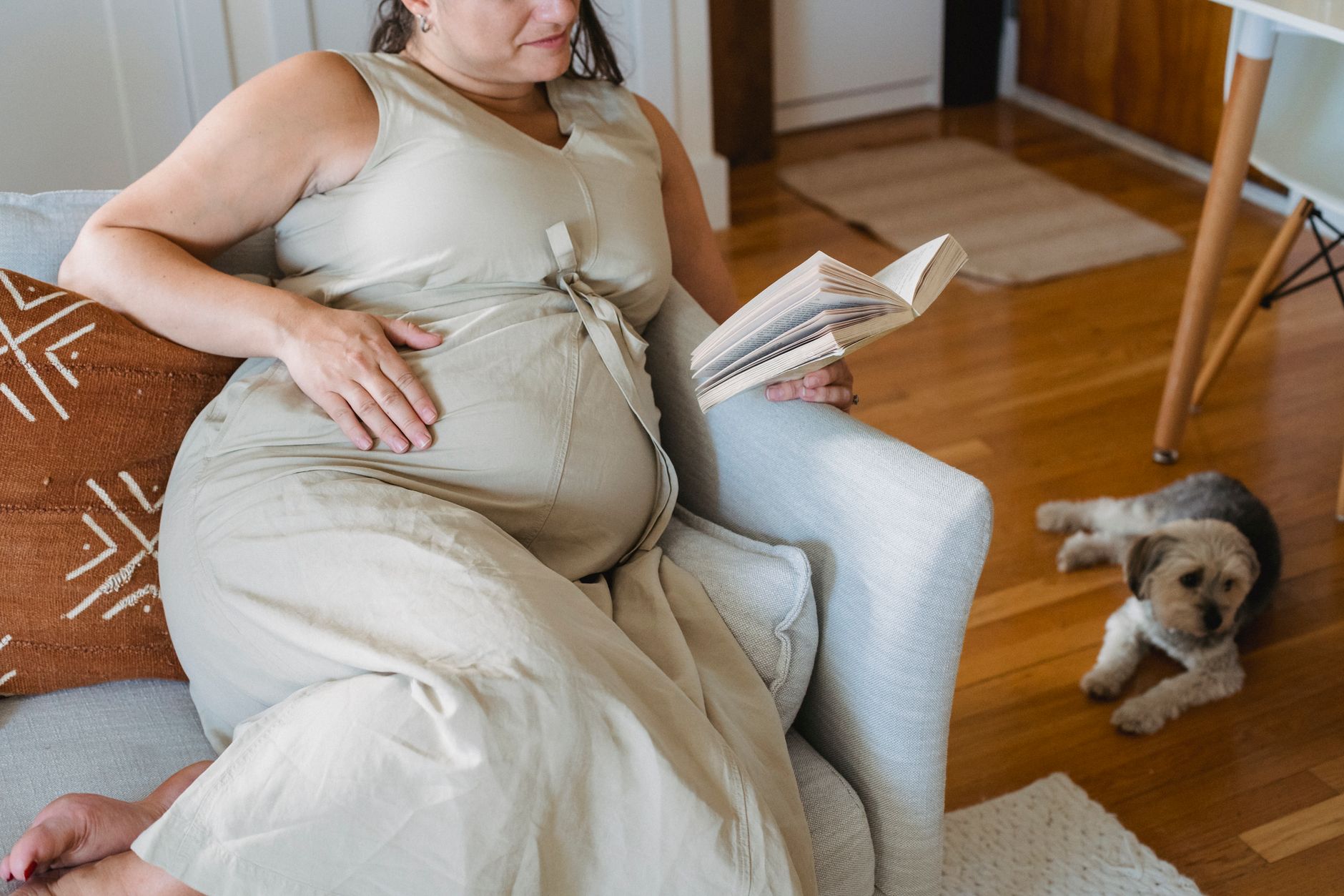 A pregnant woman sitting on a couch with her journal, surrounded by pregnancy books and a cozy blanket.