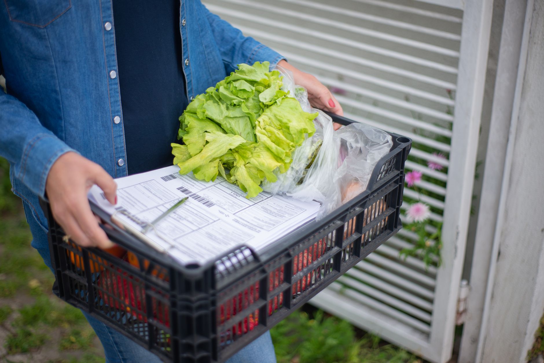 A happy mom holding a grocery delivery bag with fresh produce and her baby in a carrier.