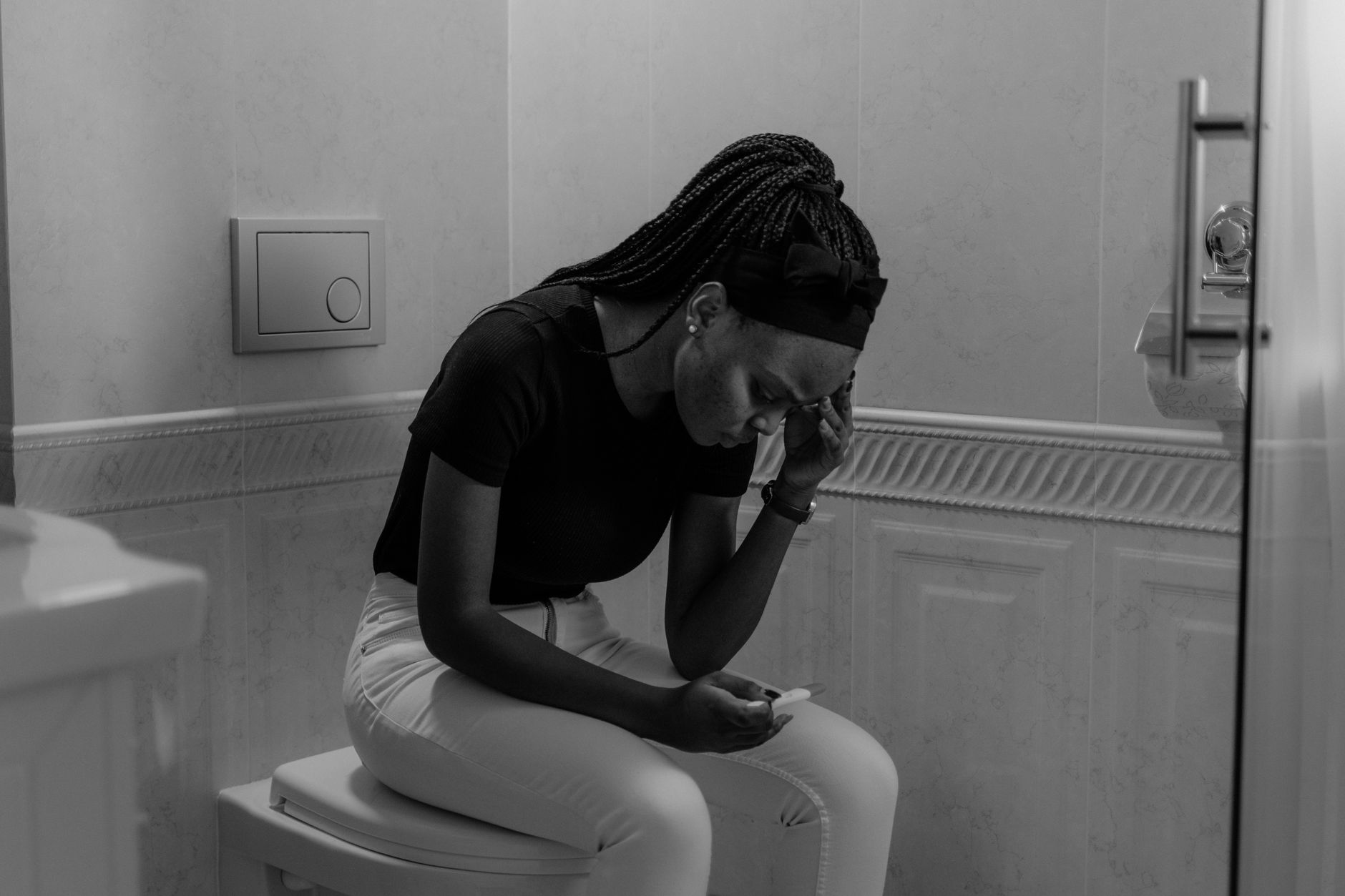 A woman holding a pregnancy test with a concerned expression, sitting on the edge of a bathtub