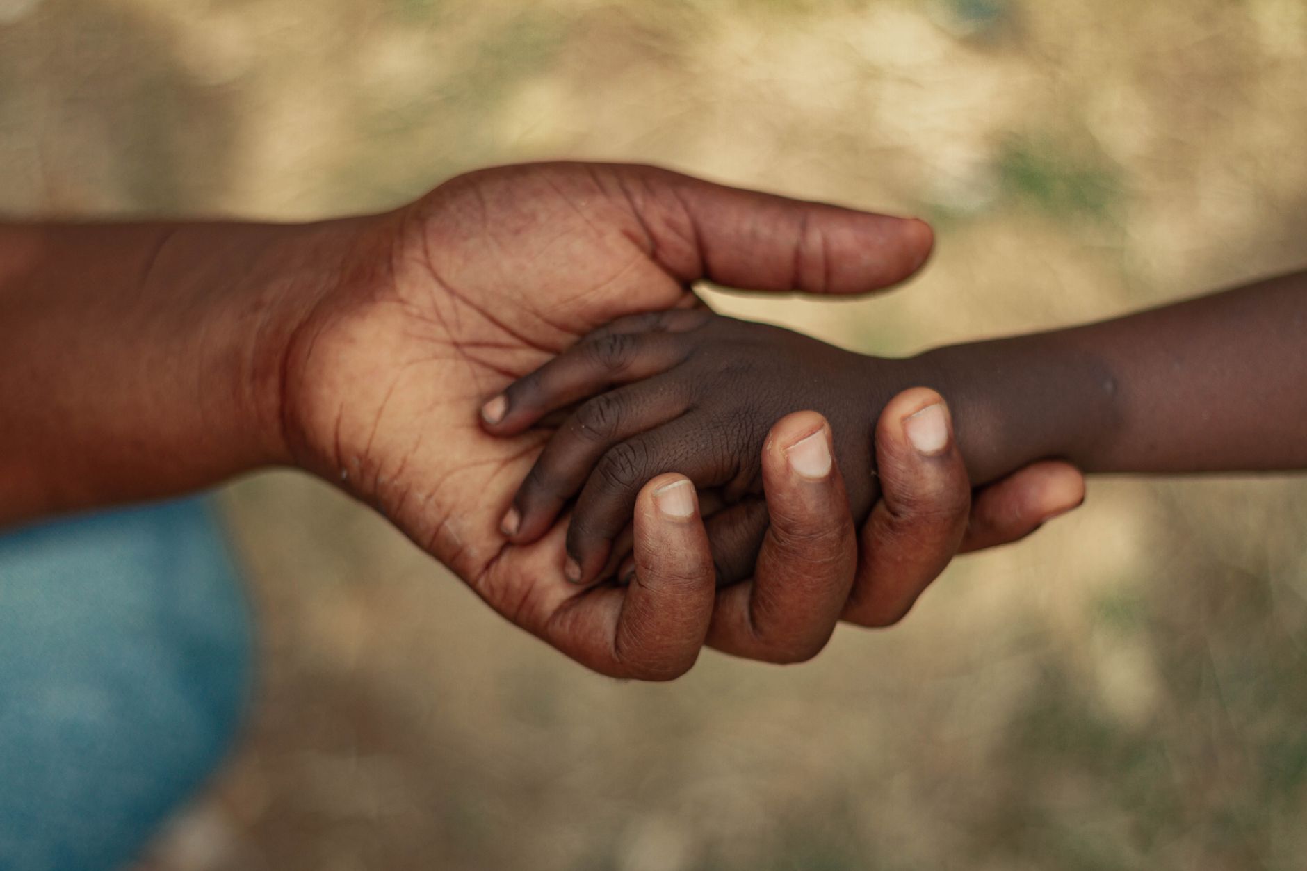 A parent's hands gently holding the hands of two different children.