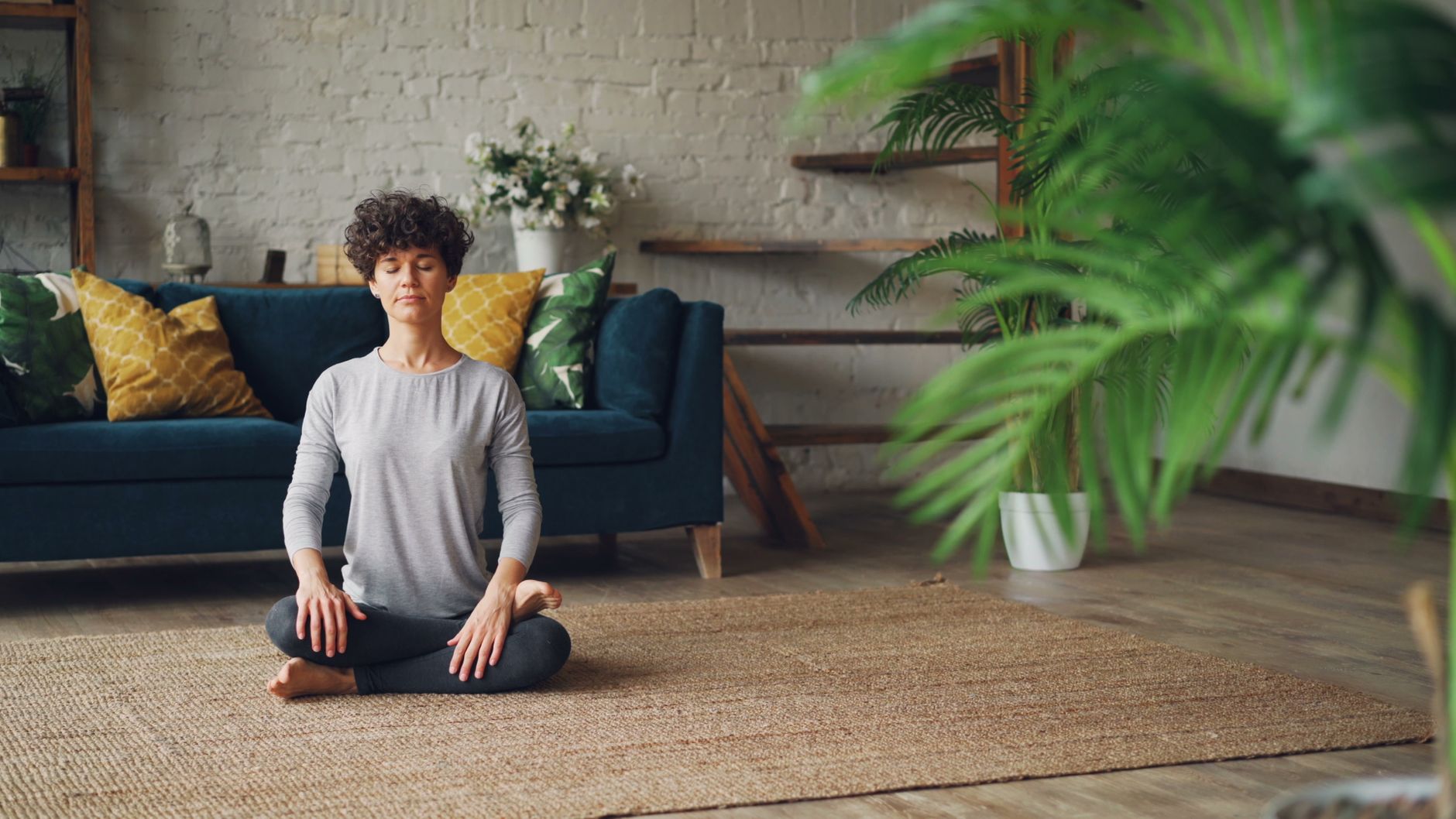 A serene woman meditating in a warm, sun-drenched room, demonstrating a moment of calm and self-care crucial for mental well-being when navigating demanding situations like coparenting after divorce.