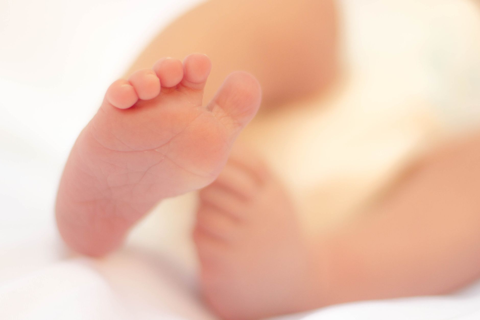 Close‑up of a newborn’s hand placed gently on a cooling cap, soft pastel background, showing the cap’s temperature sensor