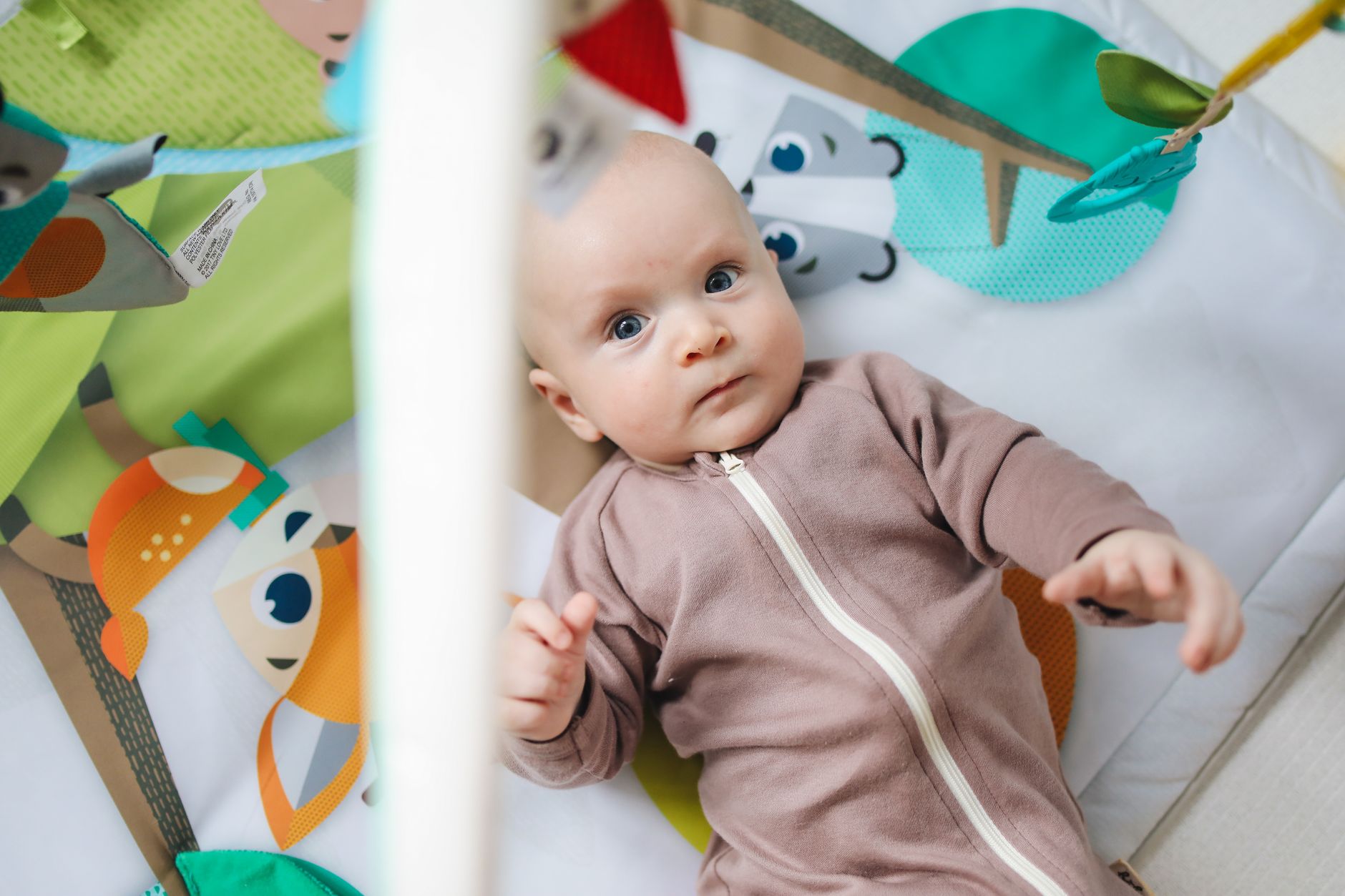 A baby lying on a playmat, kicking legs and exploring toys, demonstrating free movement