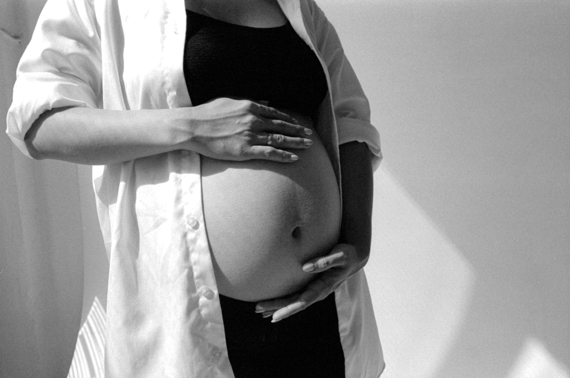 A pregnant woman's hands gently resting on her baby bump, with a kick count chart and pen nearby