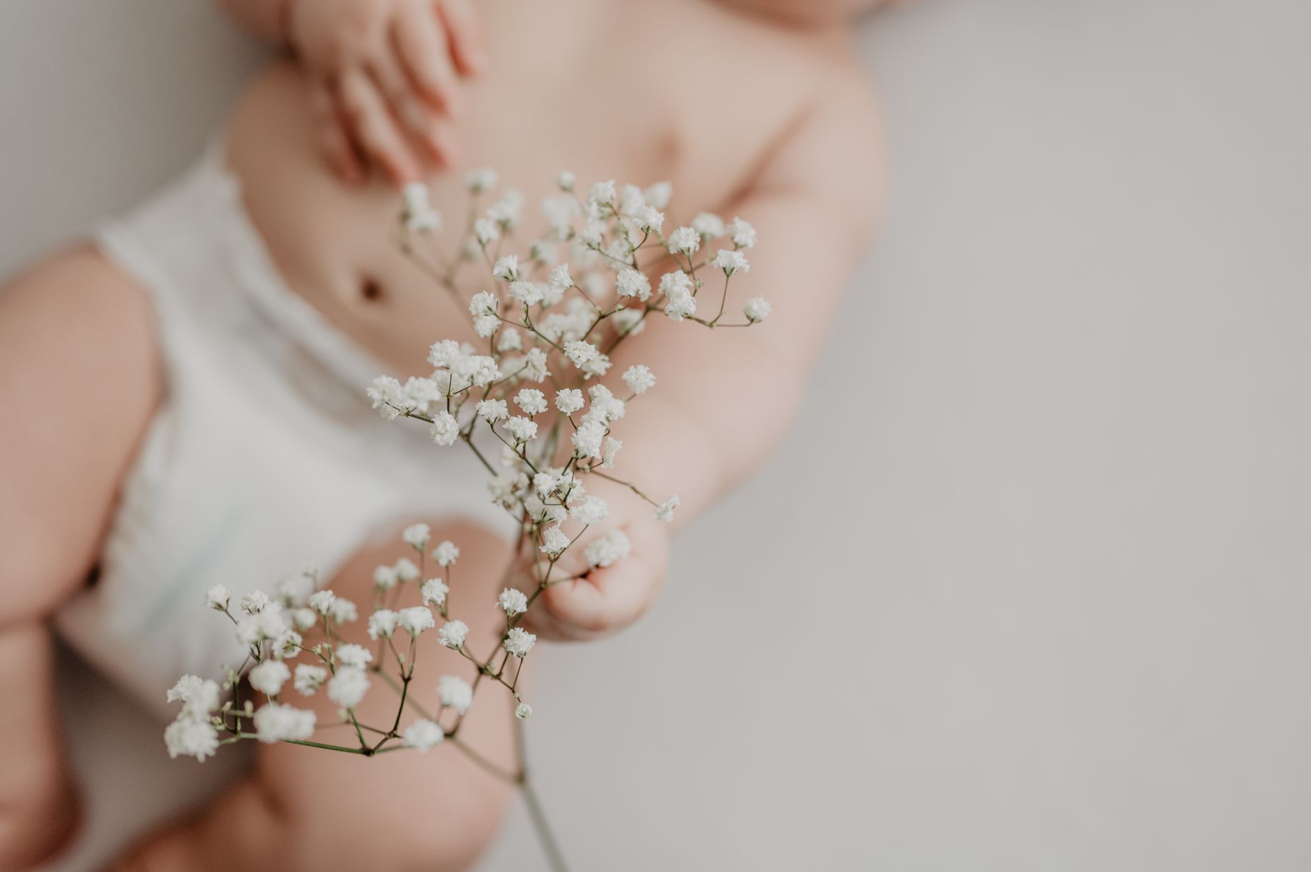 Close‑up of a newborn’s hand gently holding a soft, white diaper, highlighting the texture and gentle care involved in diaper changes