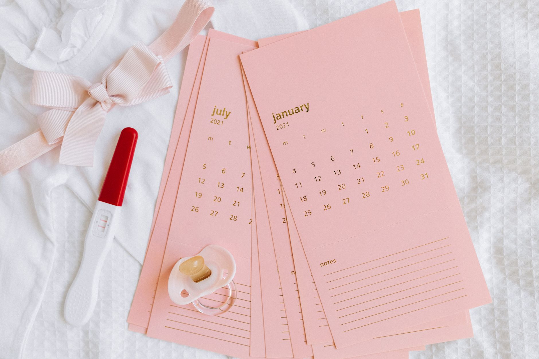 A calendar with a red circle around a date, next to a positive pregnancy test and a small baby shoe