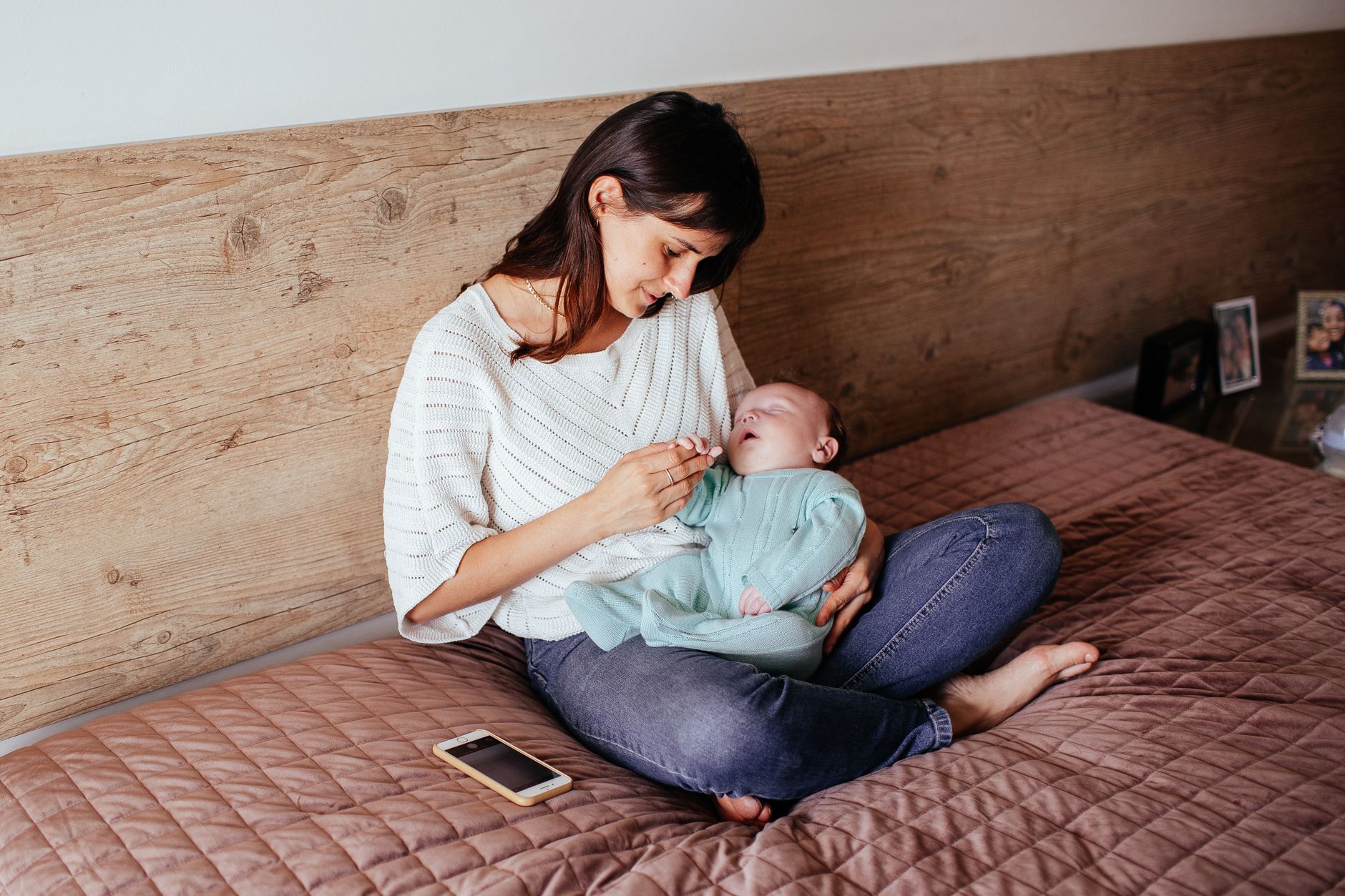 Mom holding a smartphone displaying a baby sleep tracking app, soft morning light, wooden table, cozy home setting