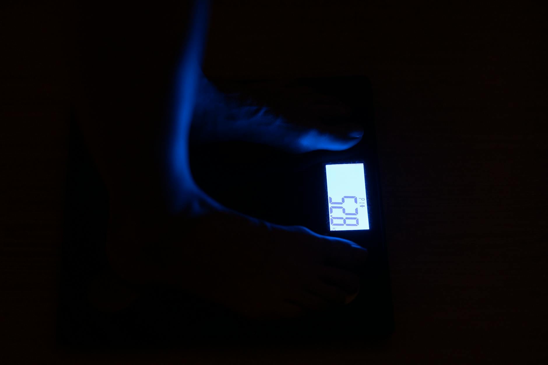 Pregnant woman stepping onto a digital scale in a bright bathroom, soft natural light, towel on the floor, calm expression