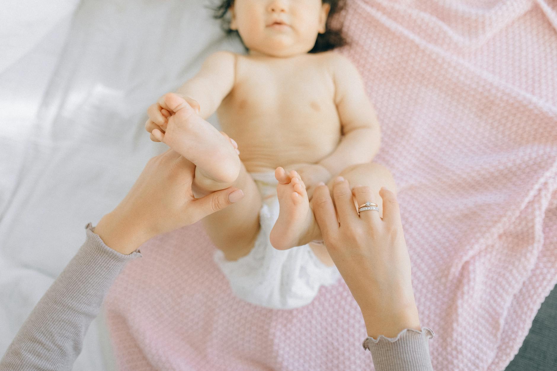 Two newborn twins lying on a soft blanket, each with a fresh diaper, surrounded by a basket of diapers and wipes