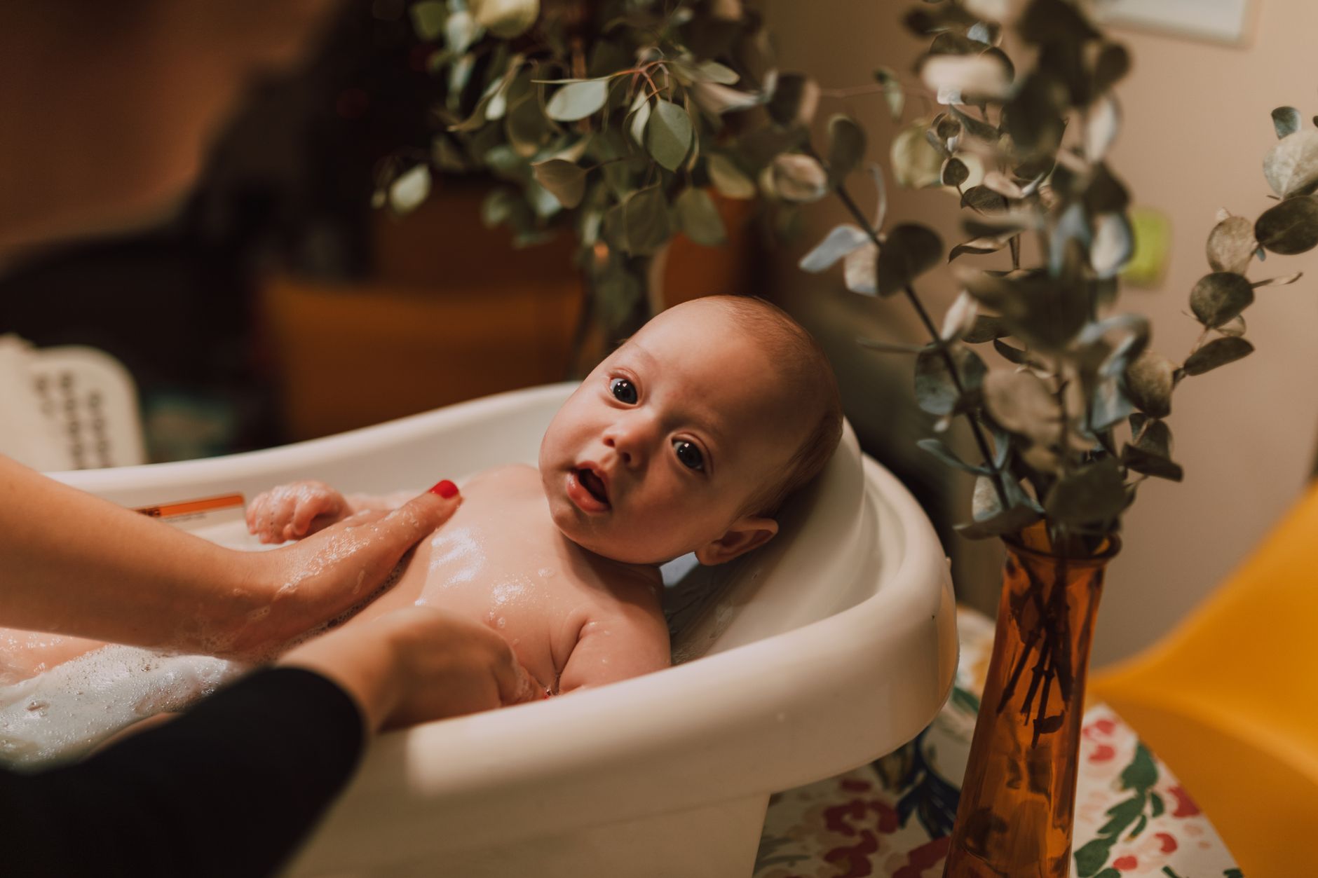 A parent's hands gently supporting a newborn baby in a small, ergonomic infant bathtub, soft focus background, warm lighting