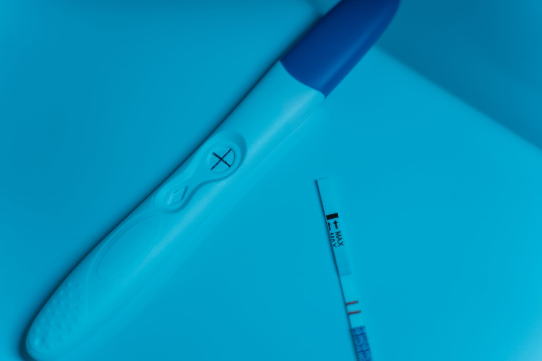 A hand holding a fertility hormone test kit next to a glass of water on a sunny kitchen counter