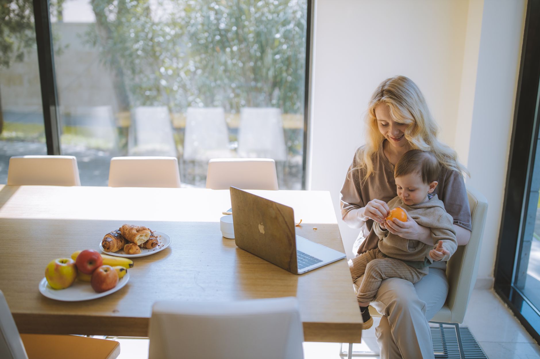A working mother balancing her baby on her lap while working from home.
