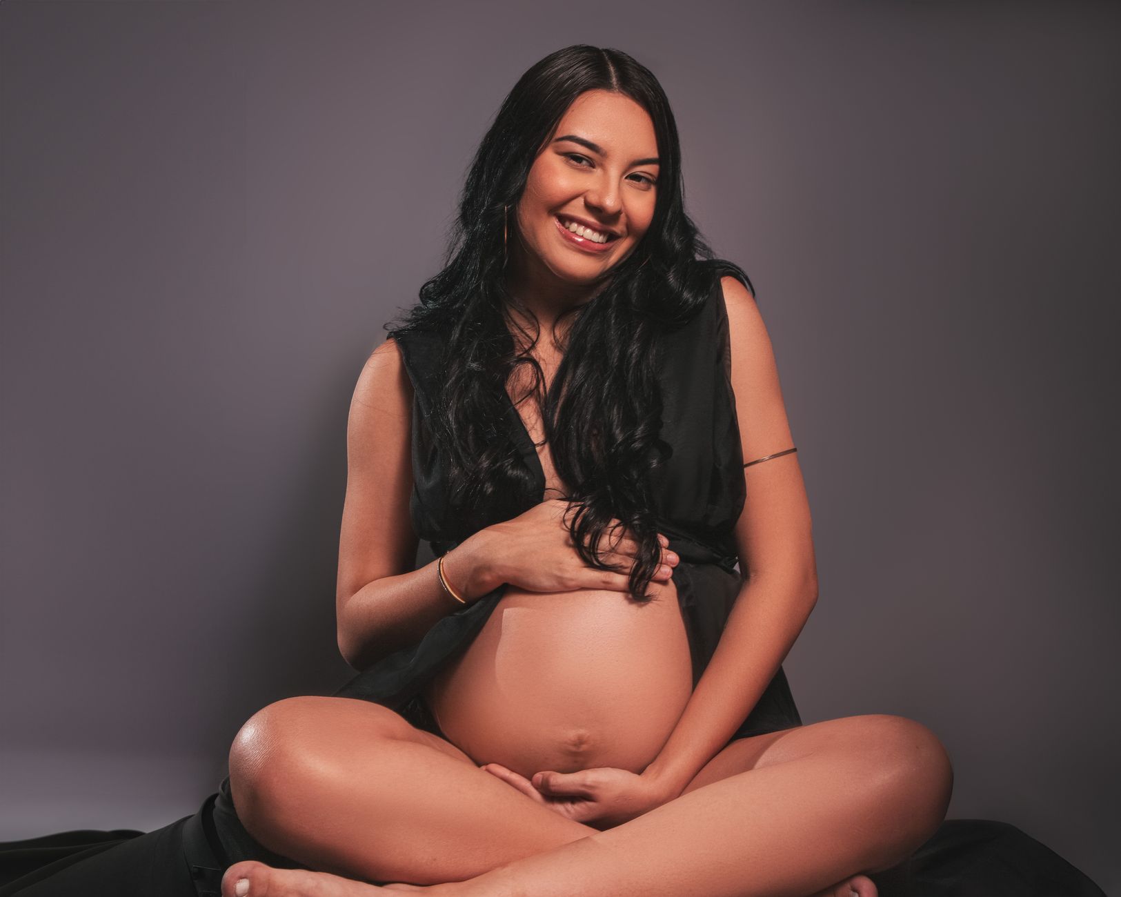 A pregnant woman placing large headphones gently on her baby bump, looking peaceful.