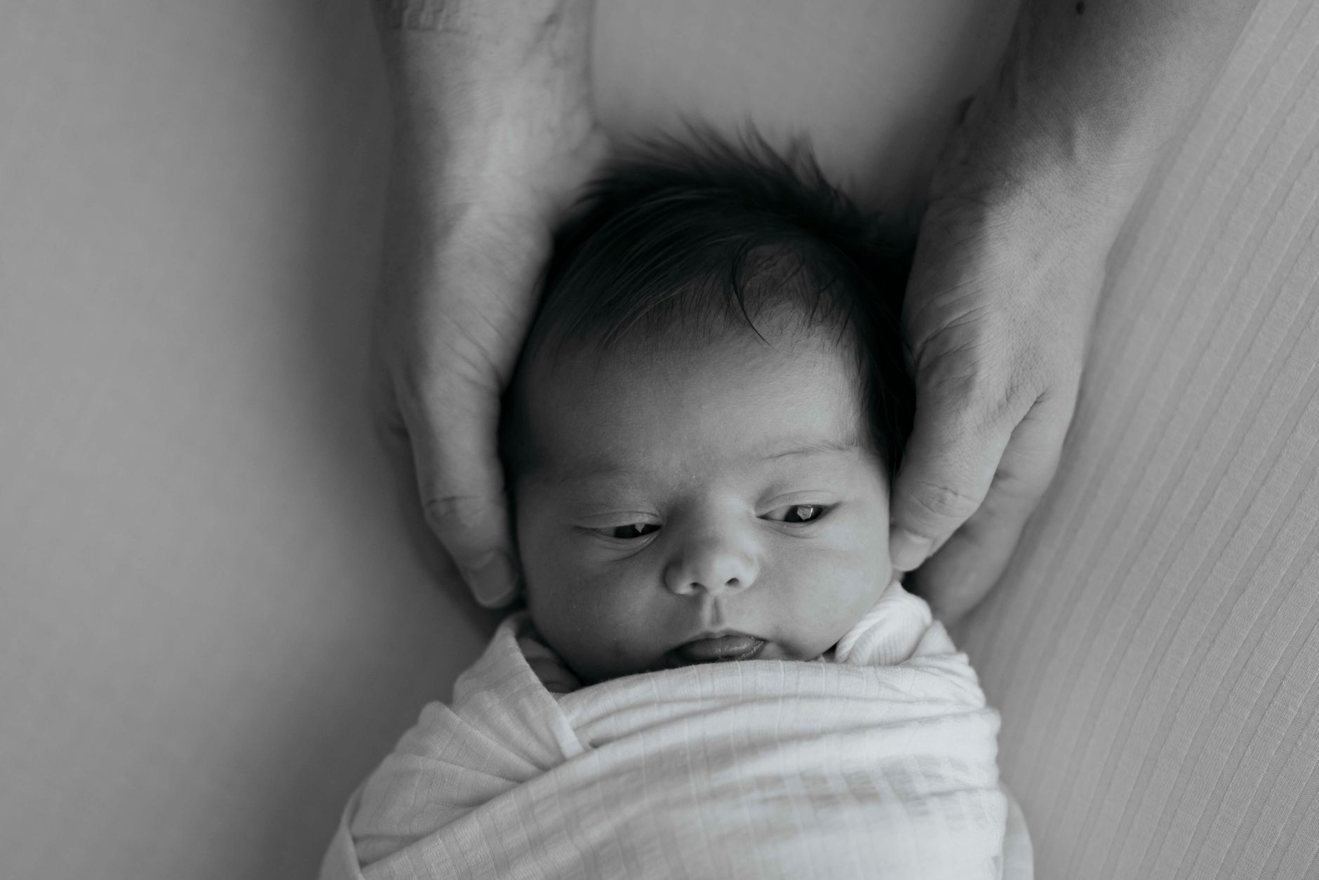 Close-up of a mother's hands gently adjusting a baby's swaddle blanket to ensure hip-healthy positioning