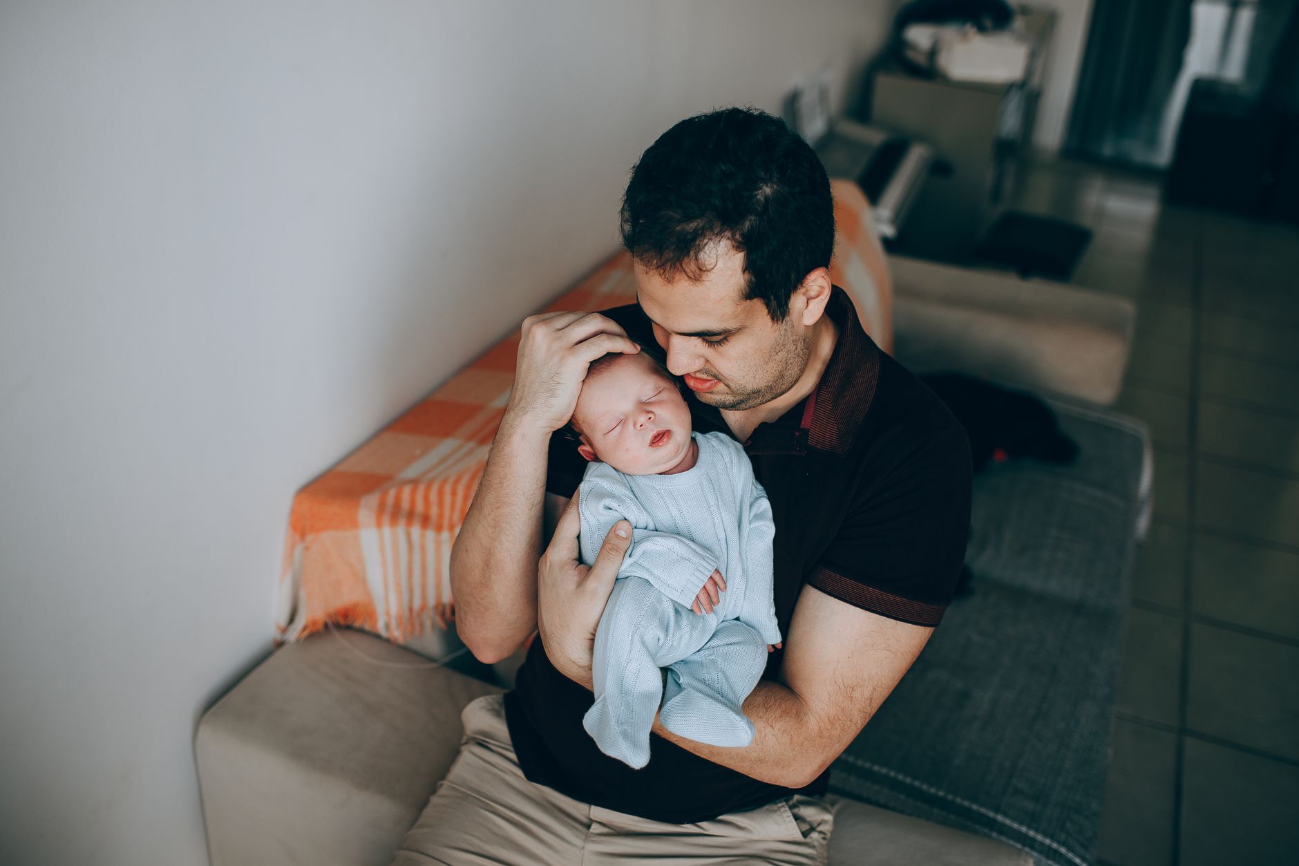 A dad sitting on a couch looking unsure as his baby cries in his arms