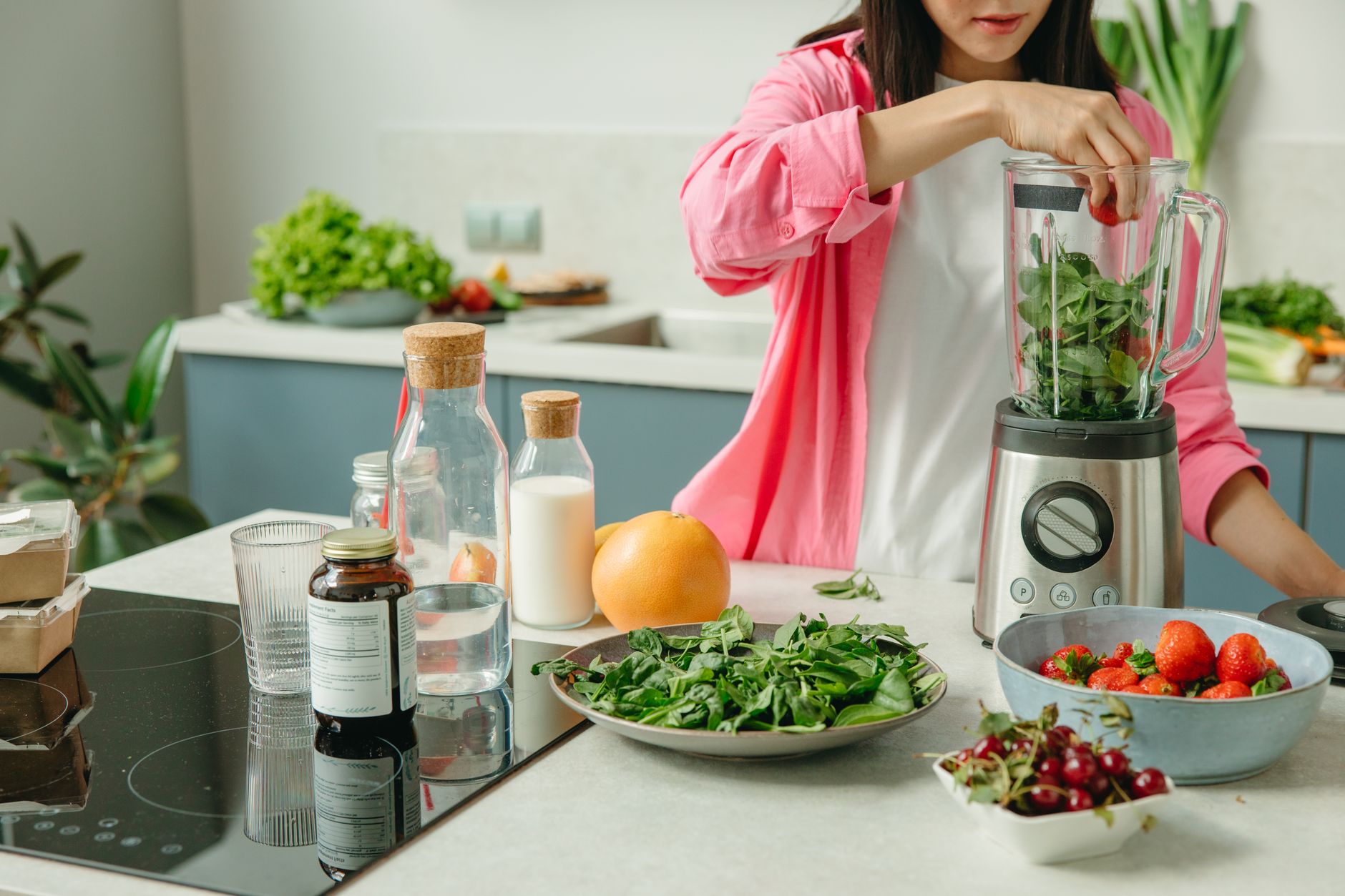 Overhead shot of a pregnant woman's hands preparing a healthy, colorful smoothie with fresh fruits and spinach, on a clean kitchen counter