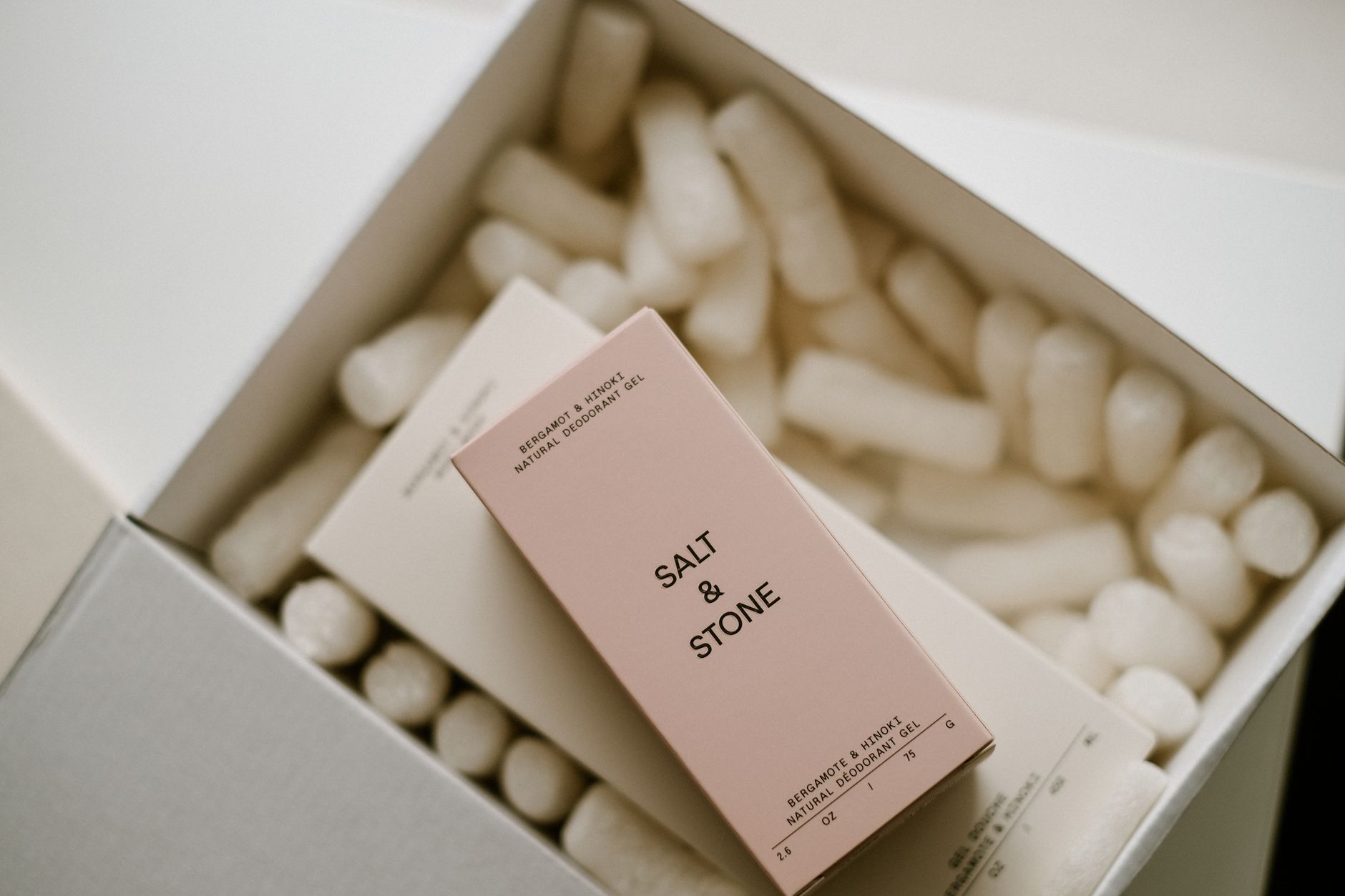 hands holding a selection of labeled deodorant sticks, some aluminum‑free, some with aluminum, set against a soft pastel background, offering a visual comparison