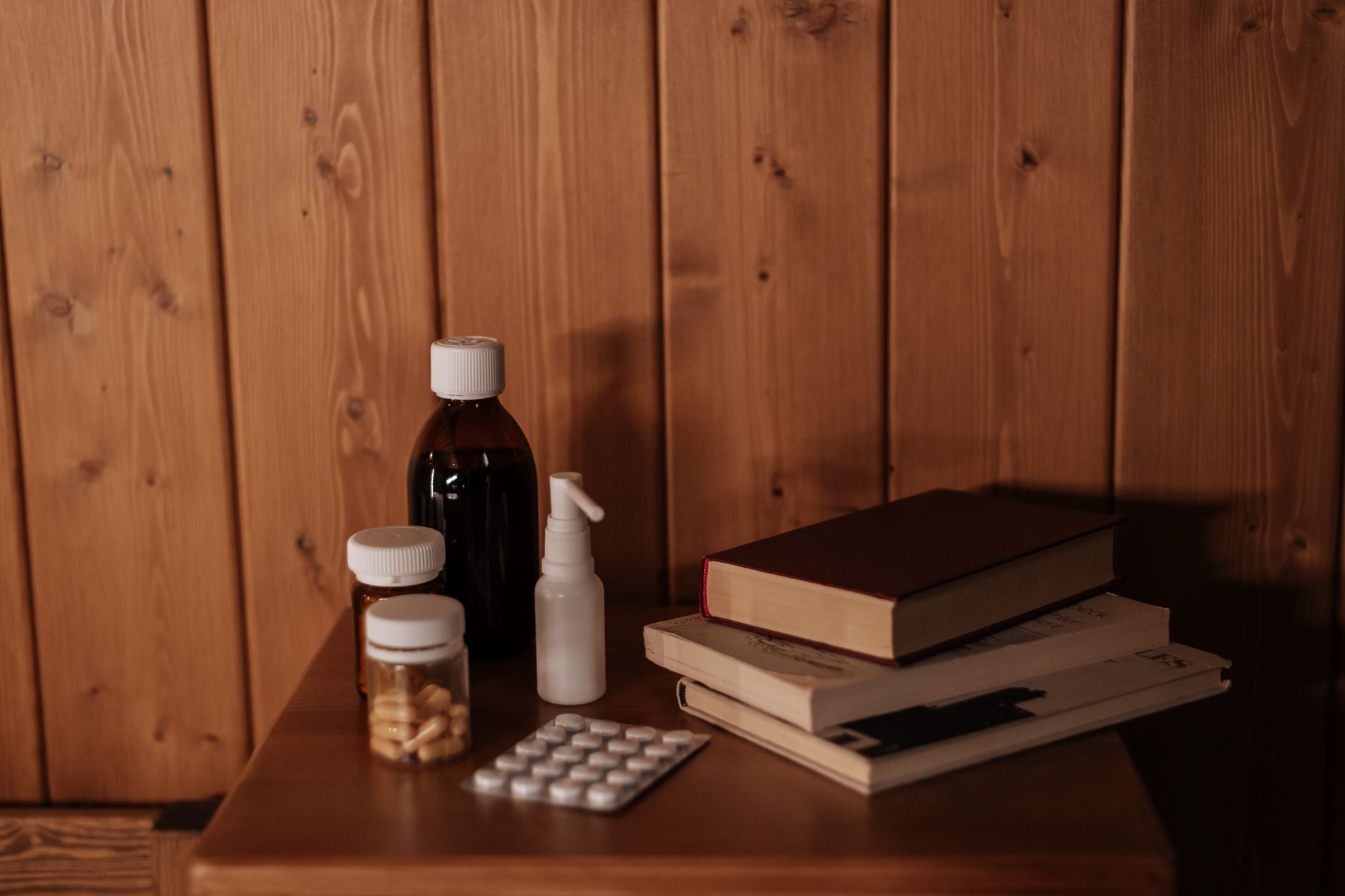 a glass of water beside a bottle of cephalexin, a small plate of cranberries, and a heating pad on a bedside table, soft morning light casting gentle shadows