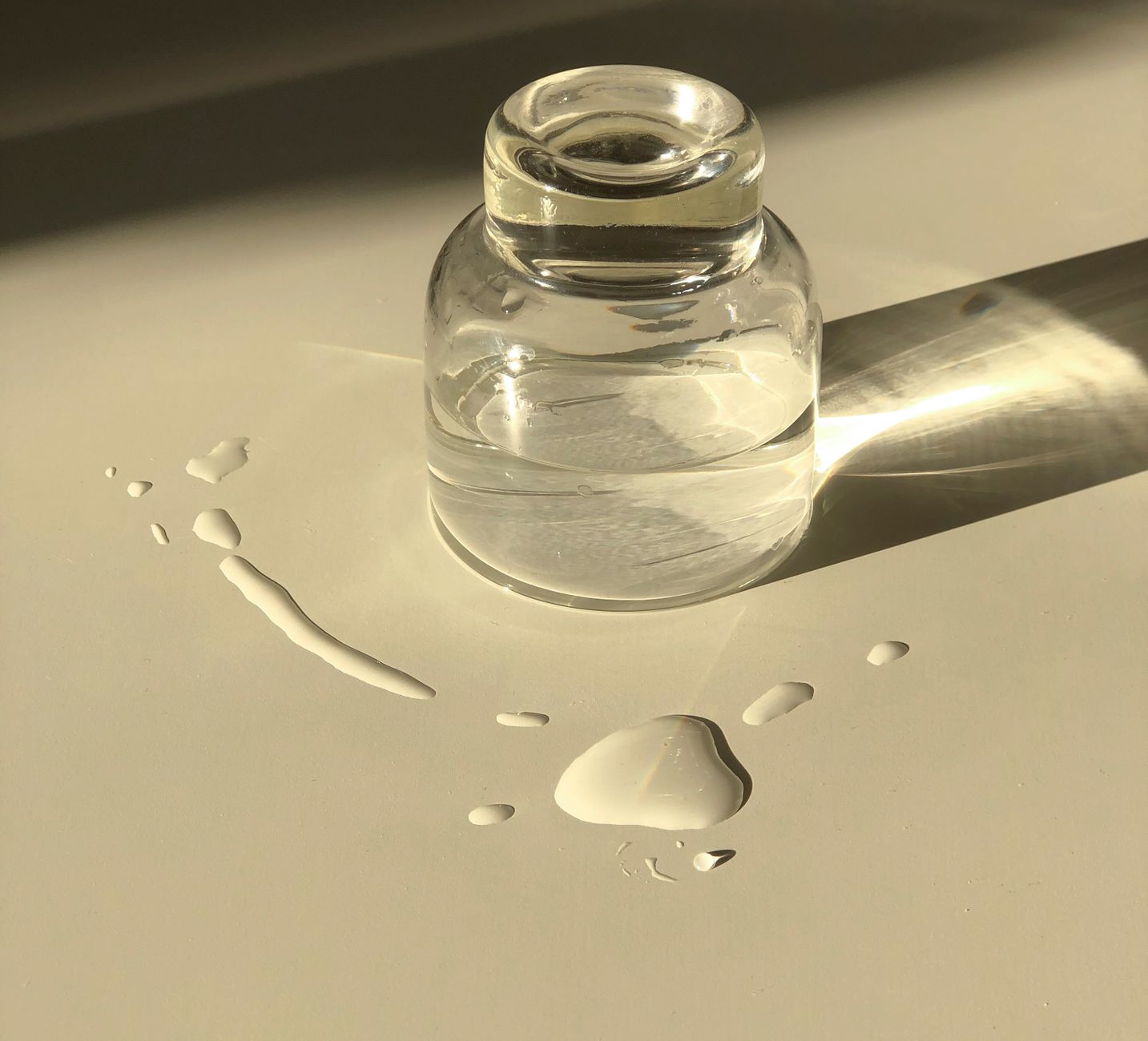 a hand holding a bottle of Tylenol next to a glass of water on a kitchen counter, bright natural lighting emphasizing the product
