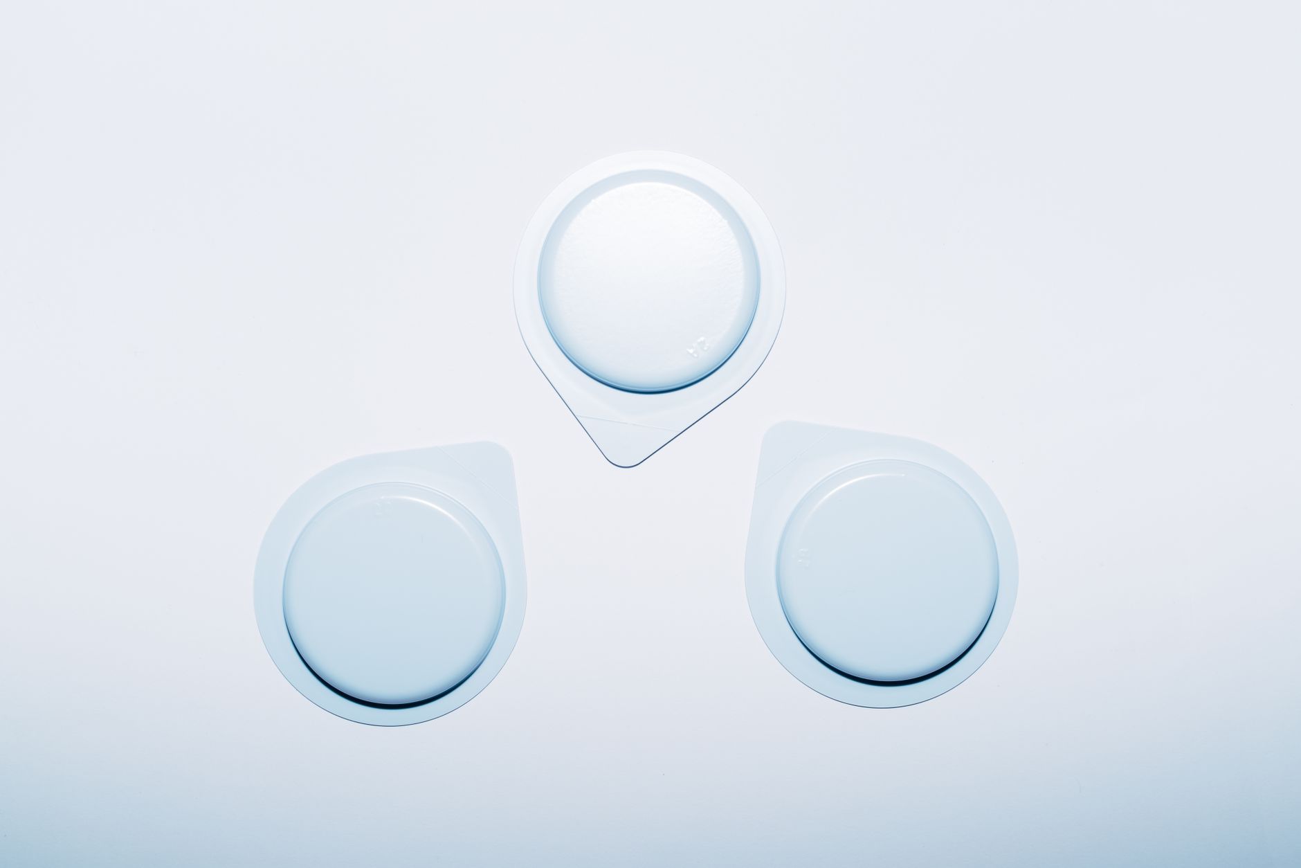 A flat lay of six pregnancy-safe lubricant bottles arranged in a circle on a soft fabric background, labeled with their names