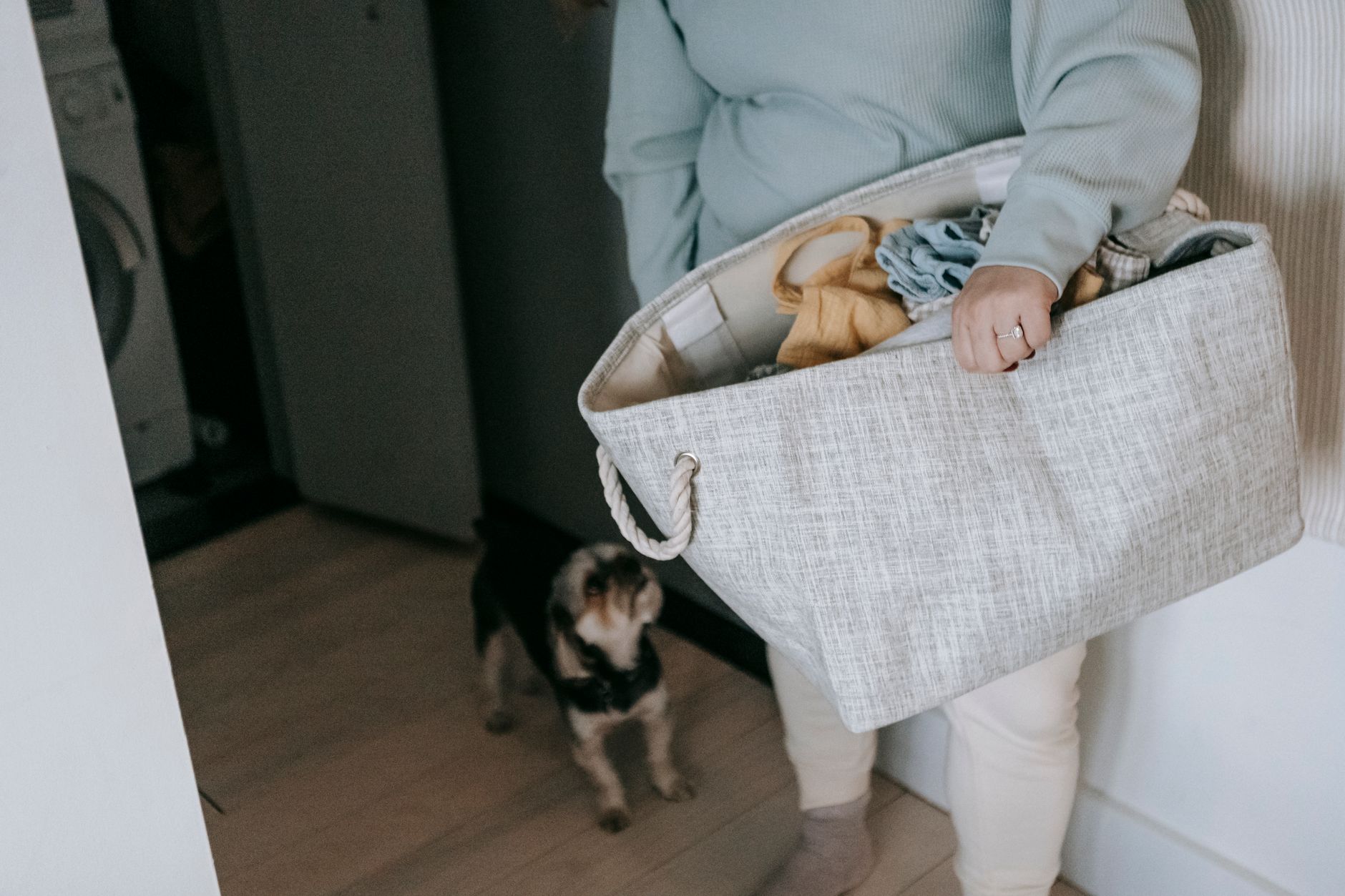 pregnant woman holding a basket of laundry next to a washing machine in a bright laundry room