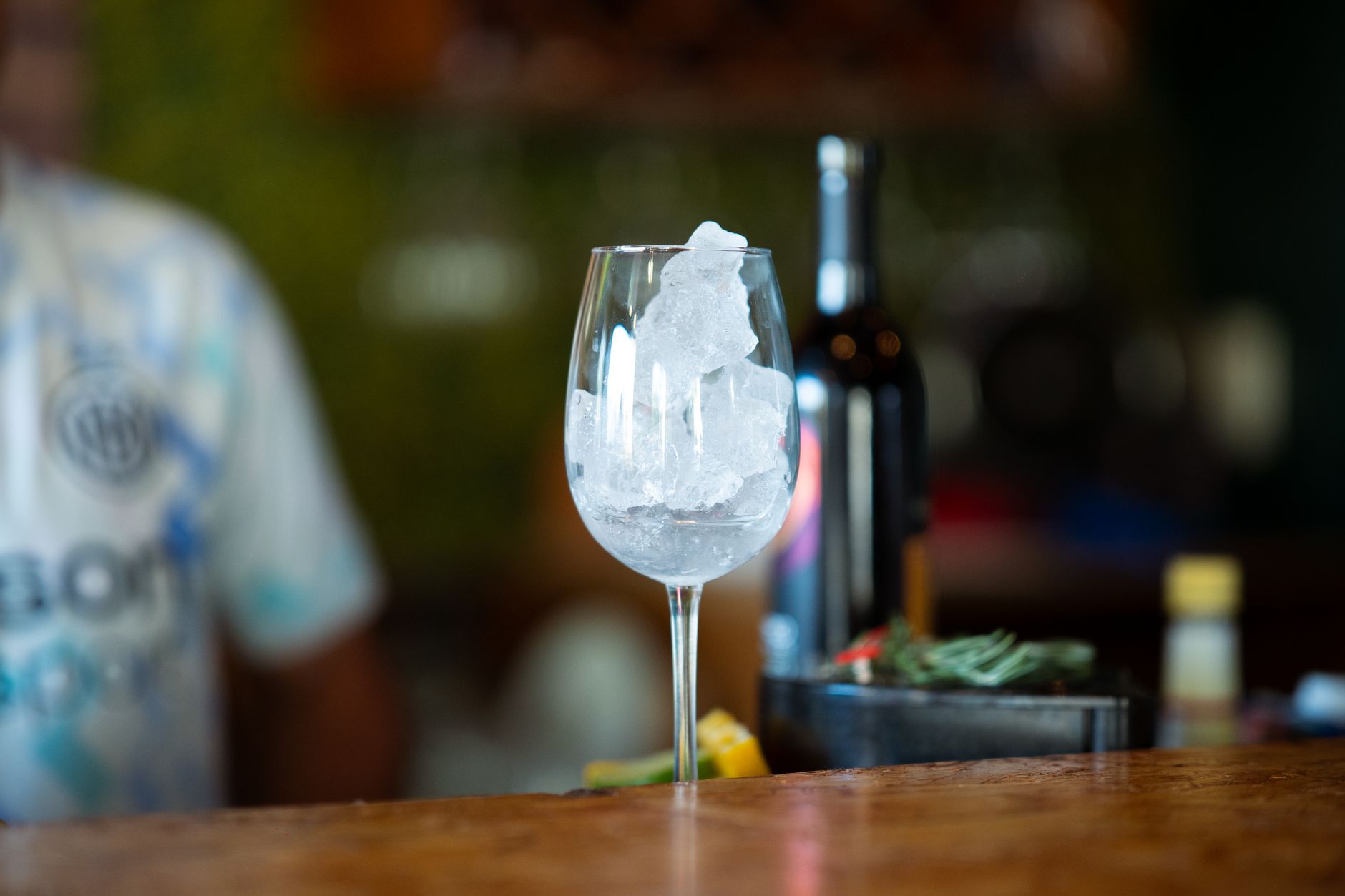 a glass of non-alcoholic red wine poured over ice with a sprig of rosemary, bright kitchen background