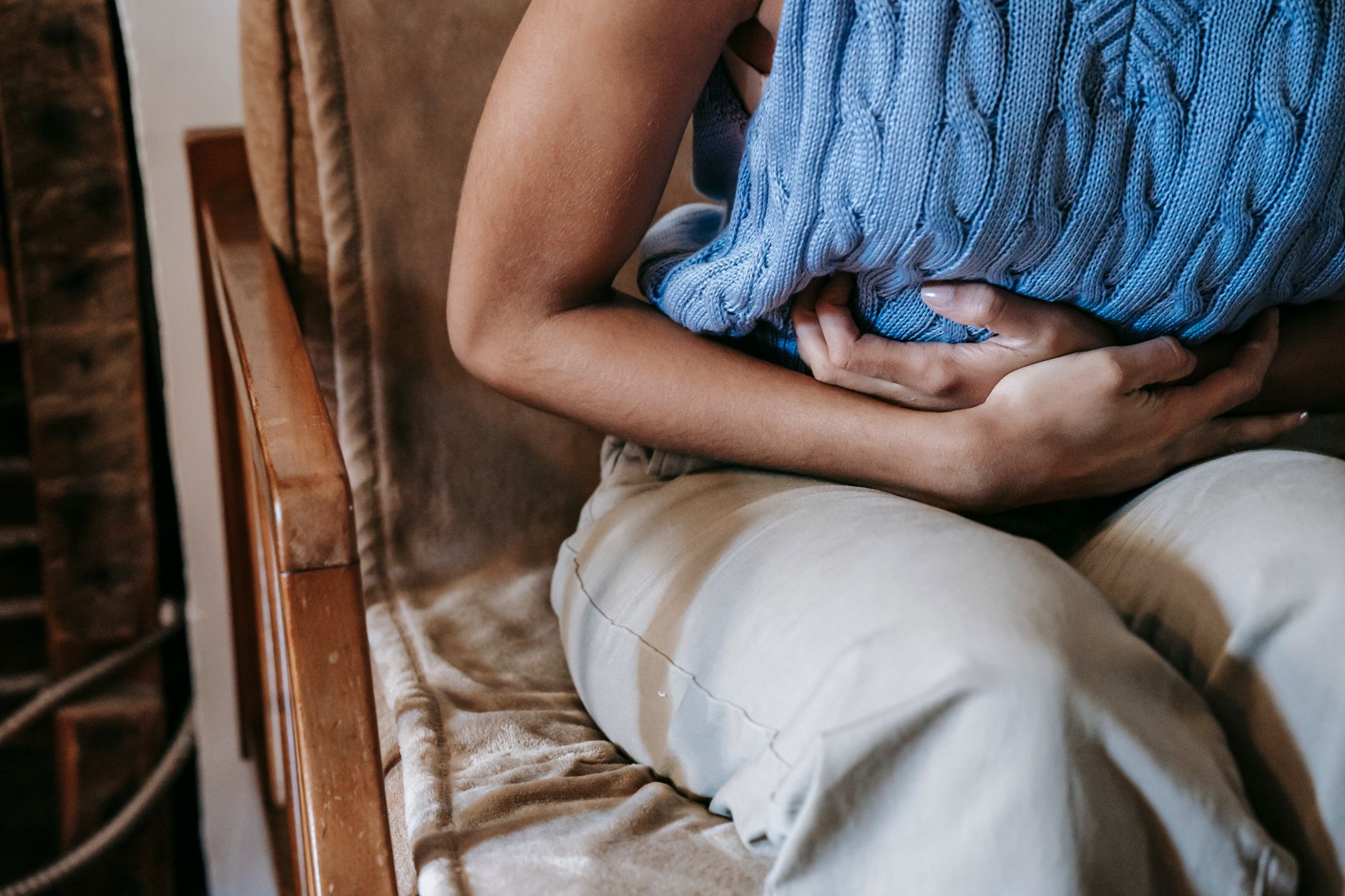 A concerned pregnant person holding their stomach, looking uncomfortable, possibly indicating digestive distress or fatigue. Soft, warm lighting, home environment. No identifiable face.