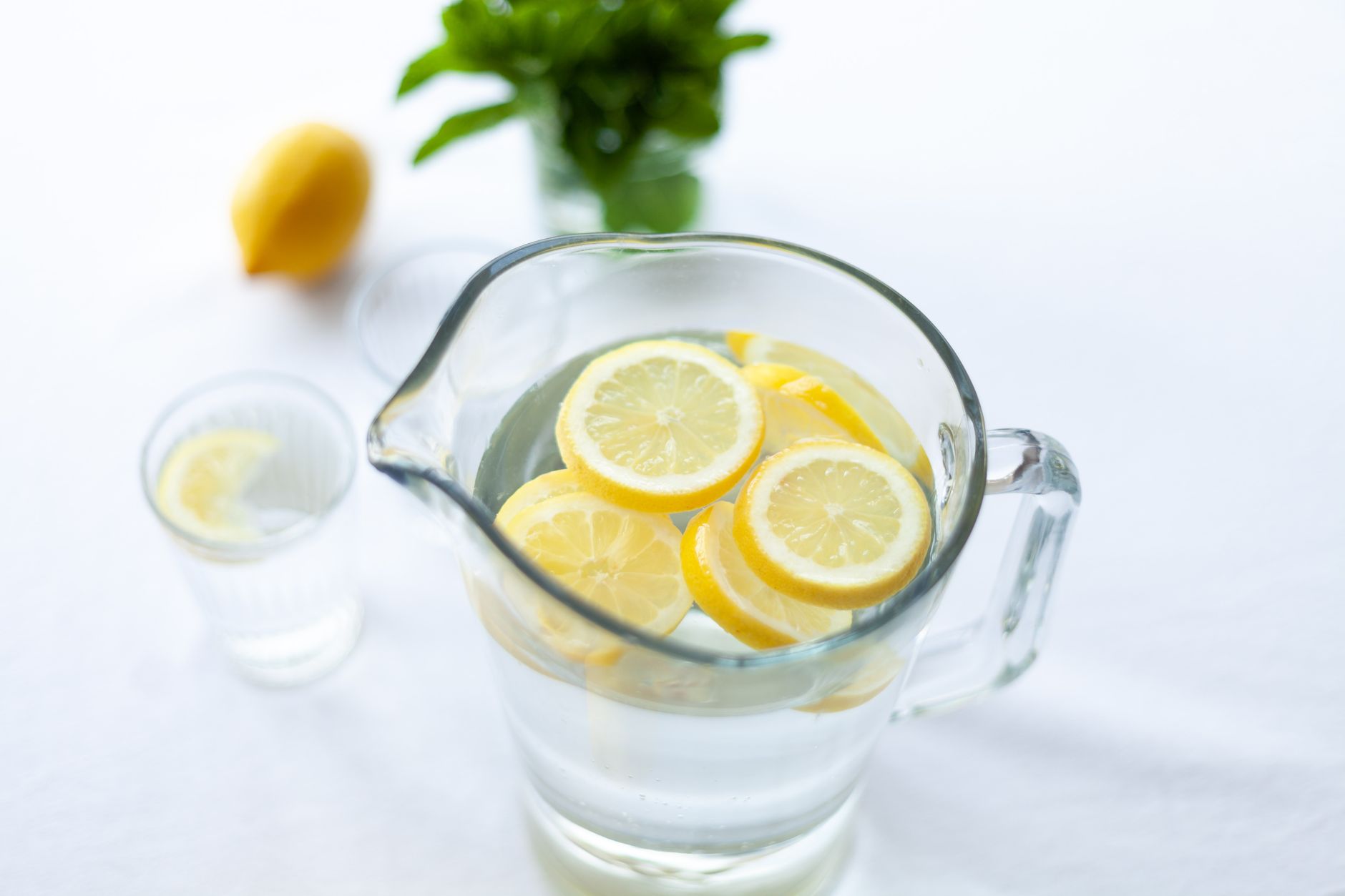 a glass of homemade lemonade on a wooden table, sliced lemons, a sprig of mint, clear sparkling water, natural light, 1200x675