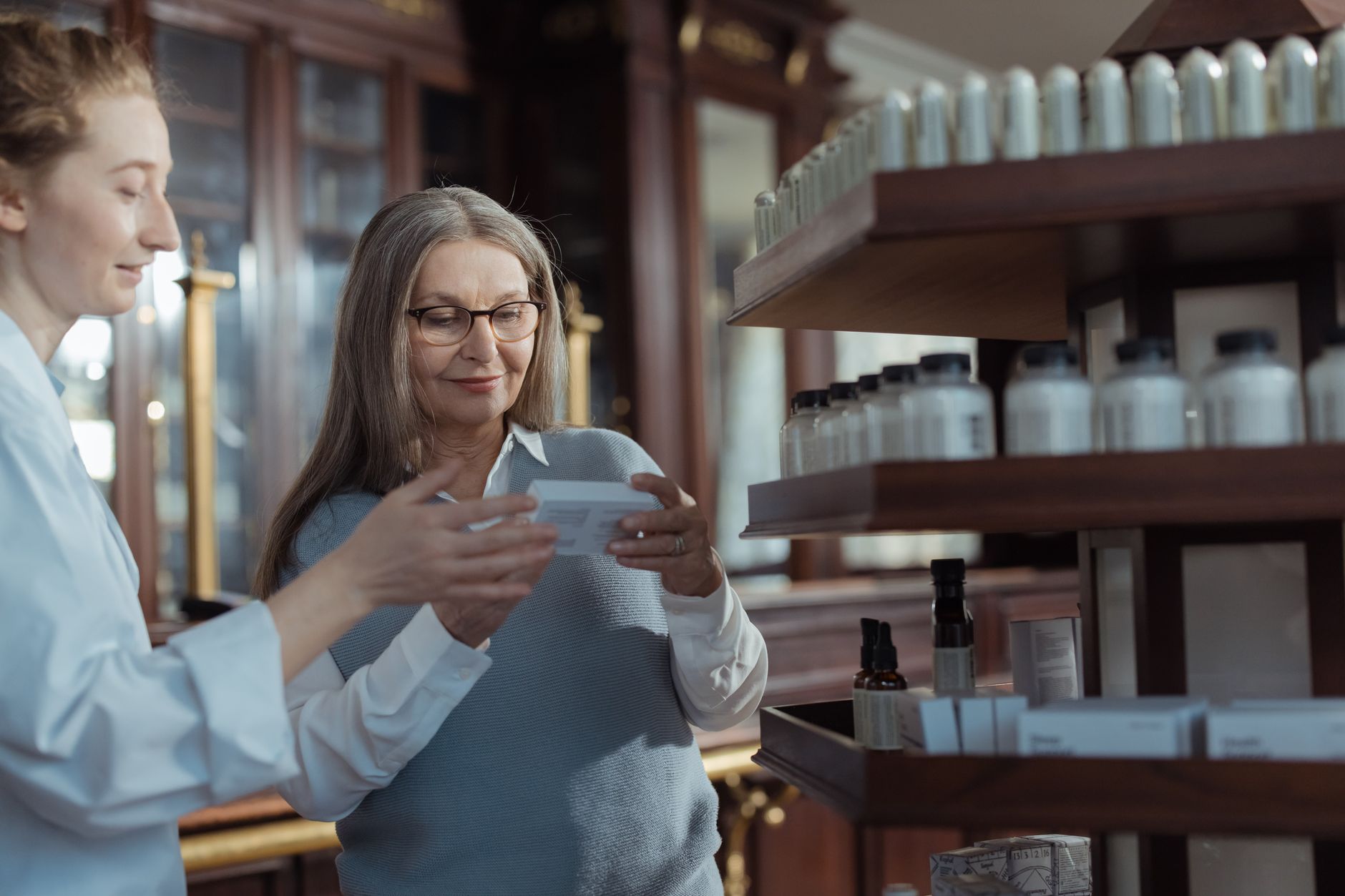 a pharmacist helping a pregnant customer choose a cough medicine, showing labeled shelves and a friendly conversation