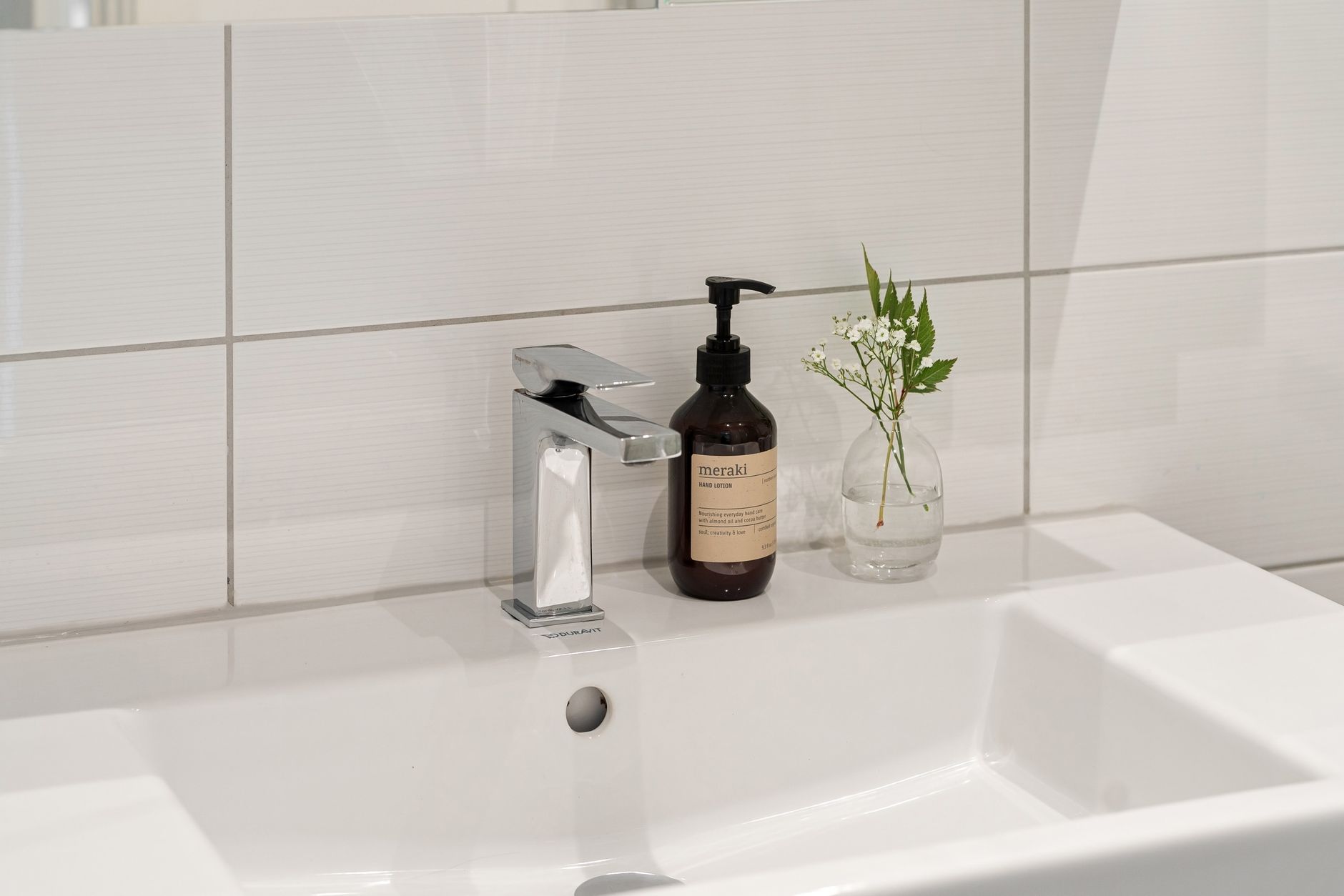 a tidy bathroom shelf holding a small bottle of pseudo‑ephedrine tablets, a glass of water, and a box of saline spray, bright natural light