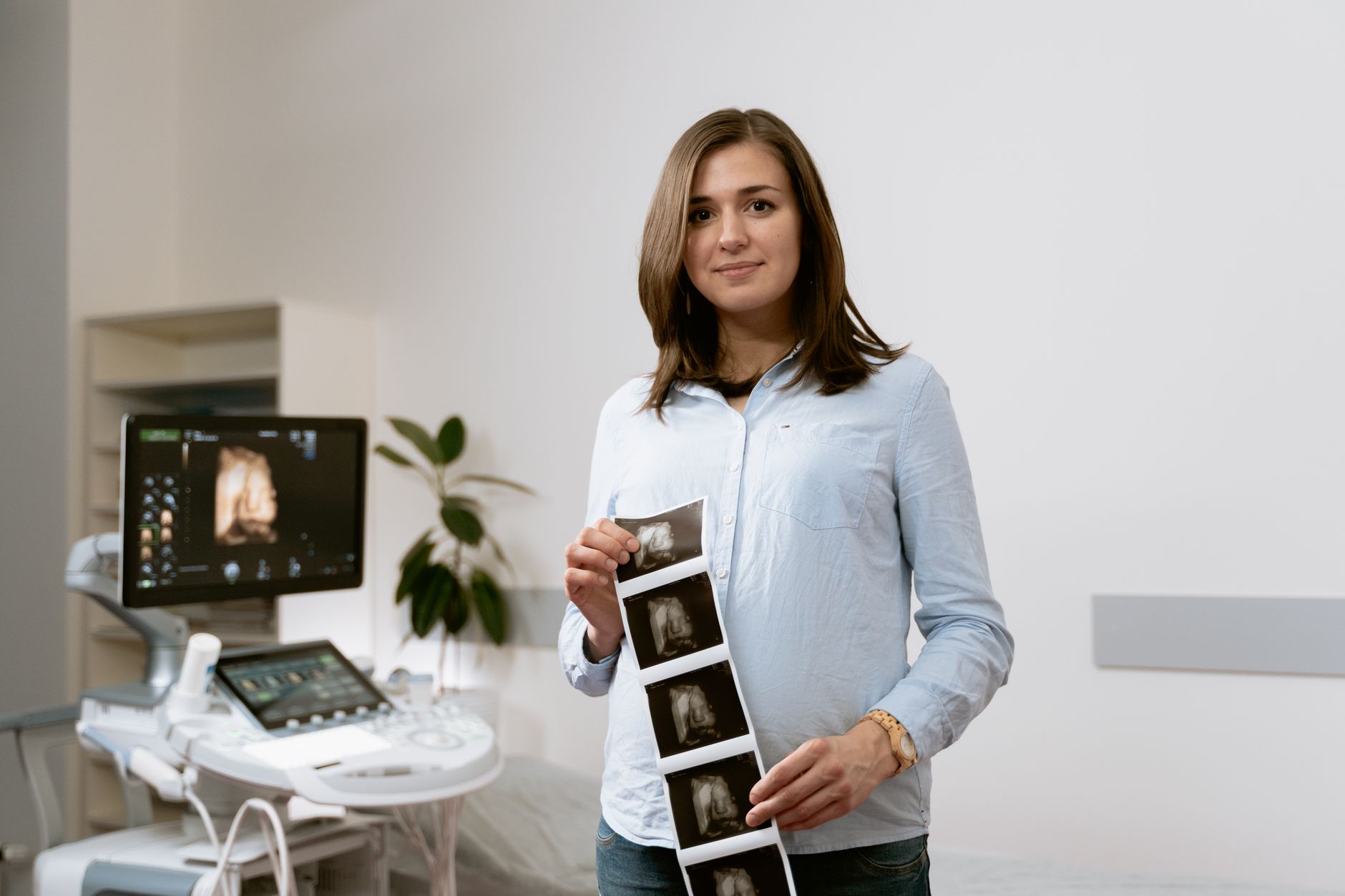 A pregnant woman holding a prenatal ultrasound image, with a small bottle of dexamethasone beside the monitor, bright clinic lighting