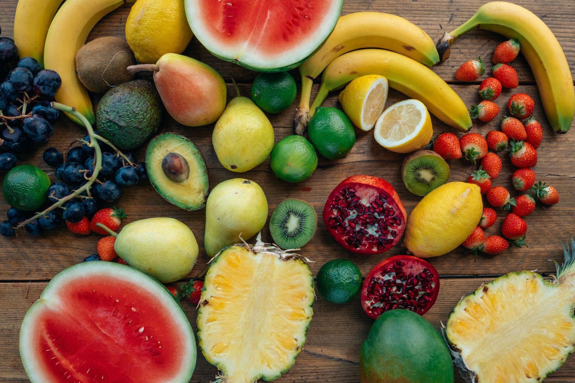 A vibrant spread of natural electrolyte-rich foods including a sliced watermelon, bananas, spinach leaves, and half an avocado, on a rustic wooden table.