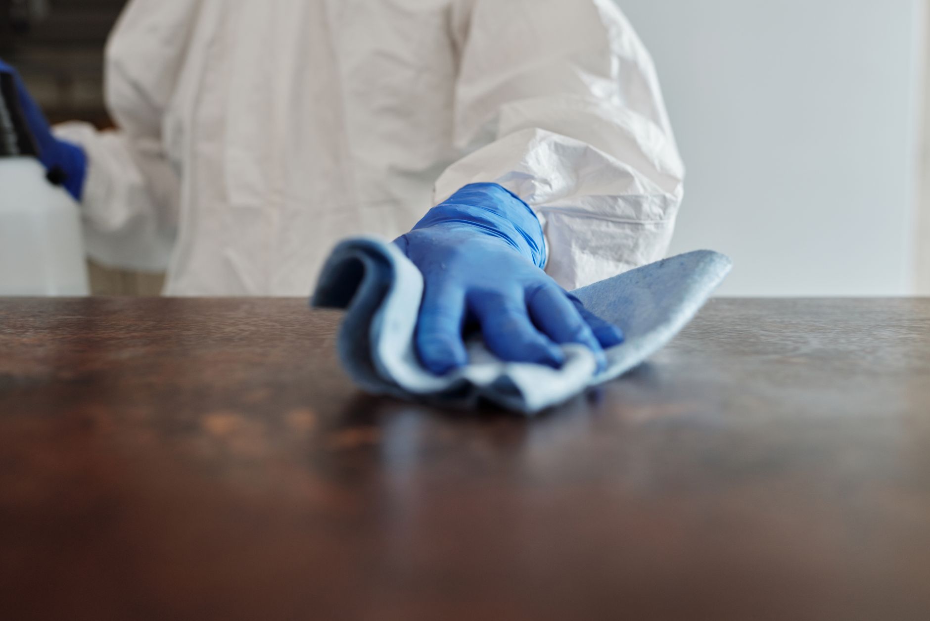 A pregnant woman wearing a face mask and gloves, standing at a distance from a child with a fever and rash, with a disinfectant wipe on a nearby surface