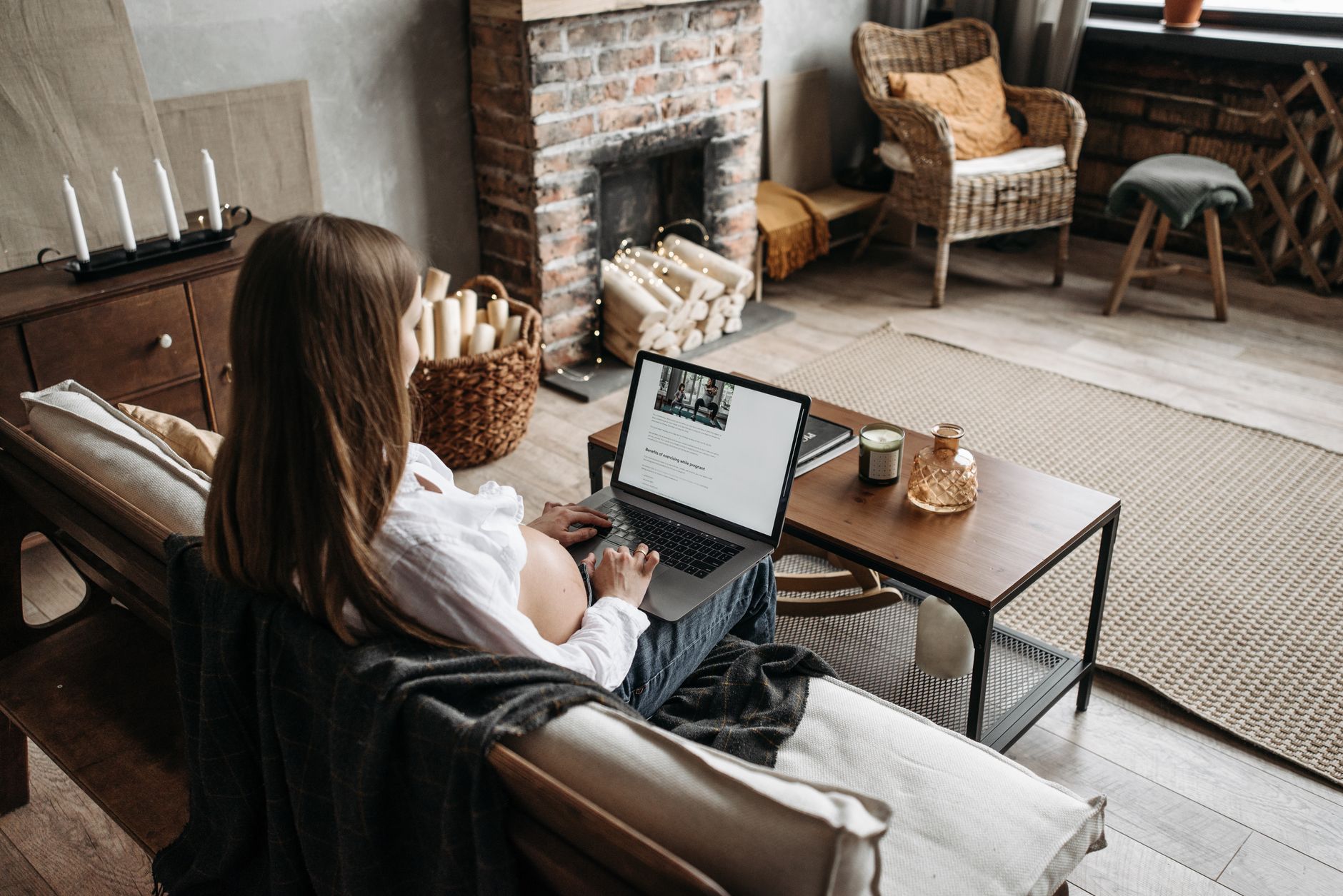 A pregnant woman sitting on a couch with a ceramic heater turned on, wrapped in a warm blanket, and using a sound machine with fireplace crackling sounds