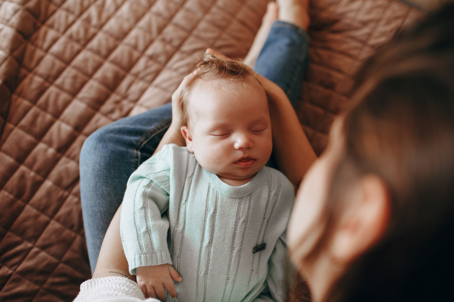 a mother holding a newborn swaddled in a blanket, both smiling, with a subtle illustration of a flu vaccine shield icon in the background, soft pastel colors