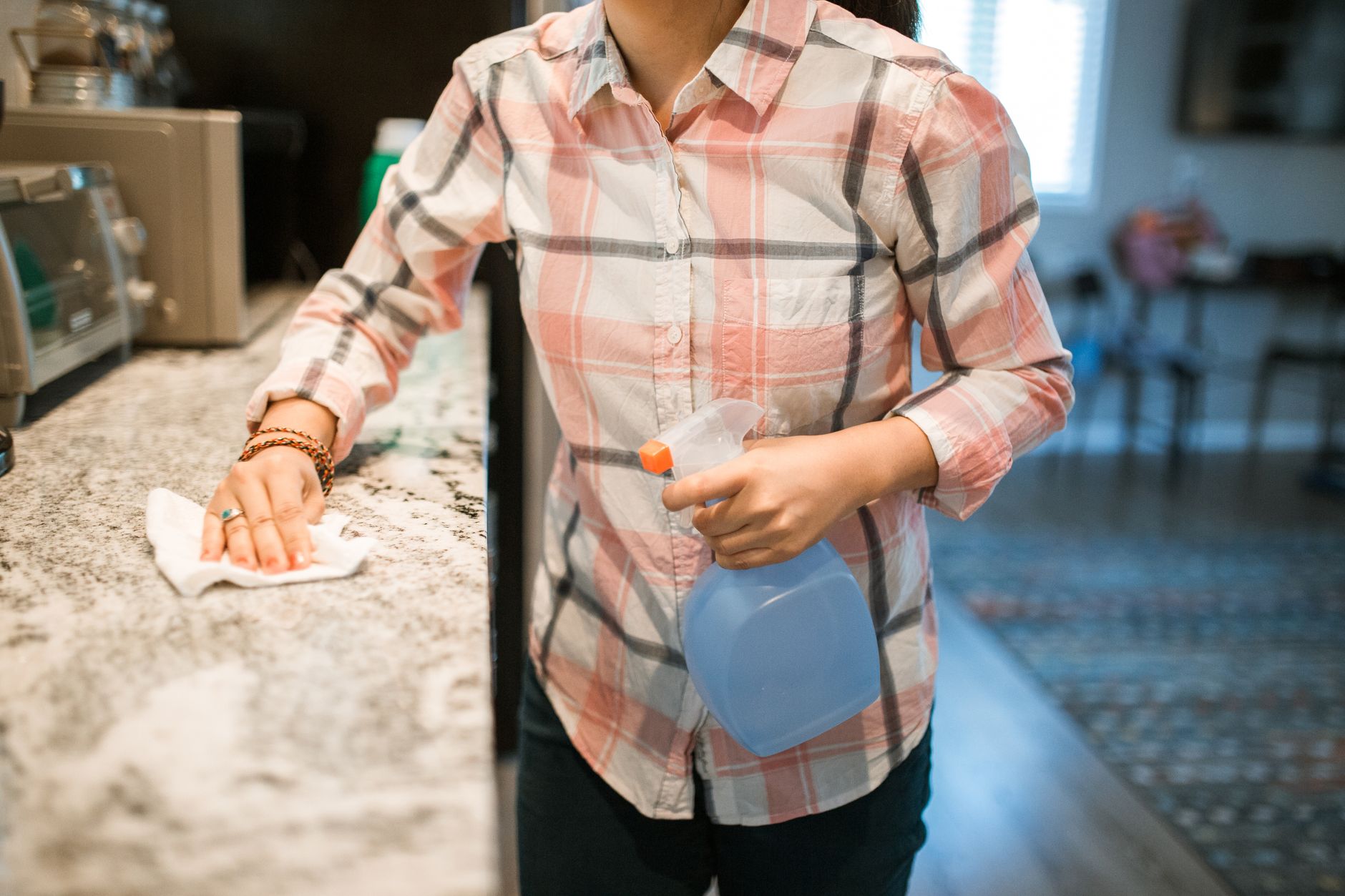 Close-up of a pregnant woman's hand gently wiping a kitchen counter with a cloth and a Force of Nature spray bottle nearby, soft focus on the hand