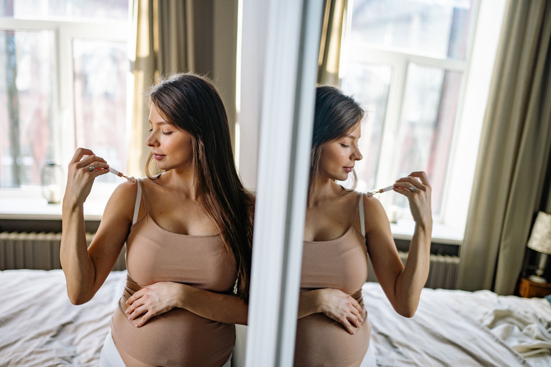 A pregnant woman gently massaging her temples in a dimly lit, comfortable bedroom, emphasizing rest and natural relief for headaches. Soft, warm light.