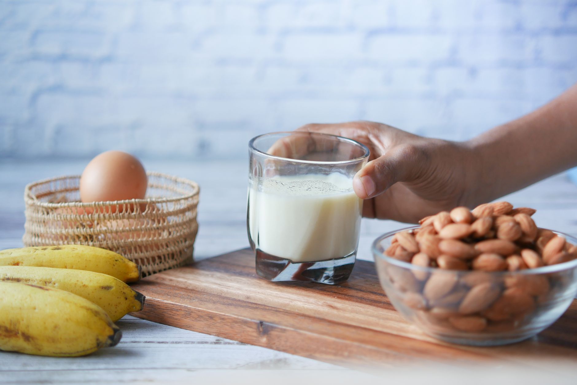 A close-up of a hand pouring a pregnancy-safe protein shake into a glass, with a spoonful of almond butter on the side and a bowl of mixed nuts