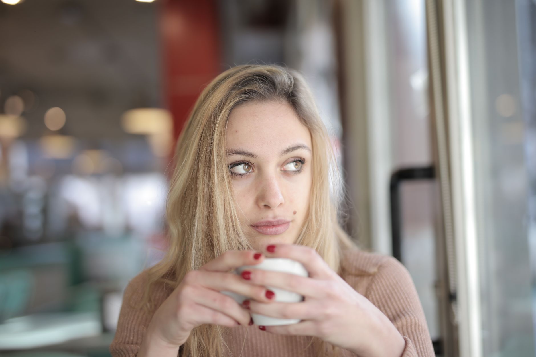 a pregnant person holding a steaming mug, looking thoughtful, with a blurred background of a cozy living room