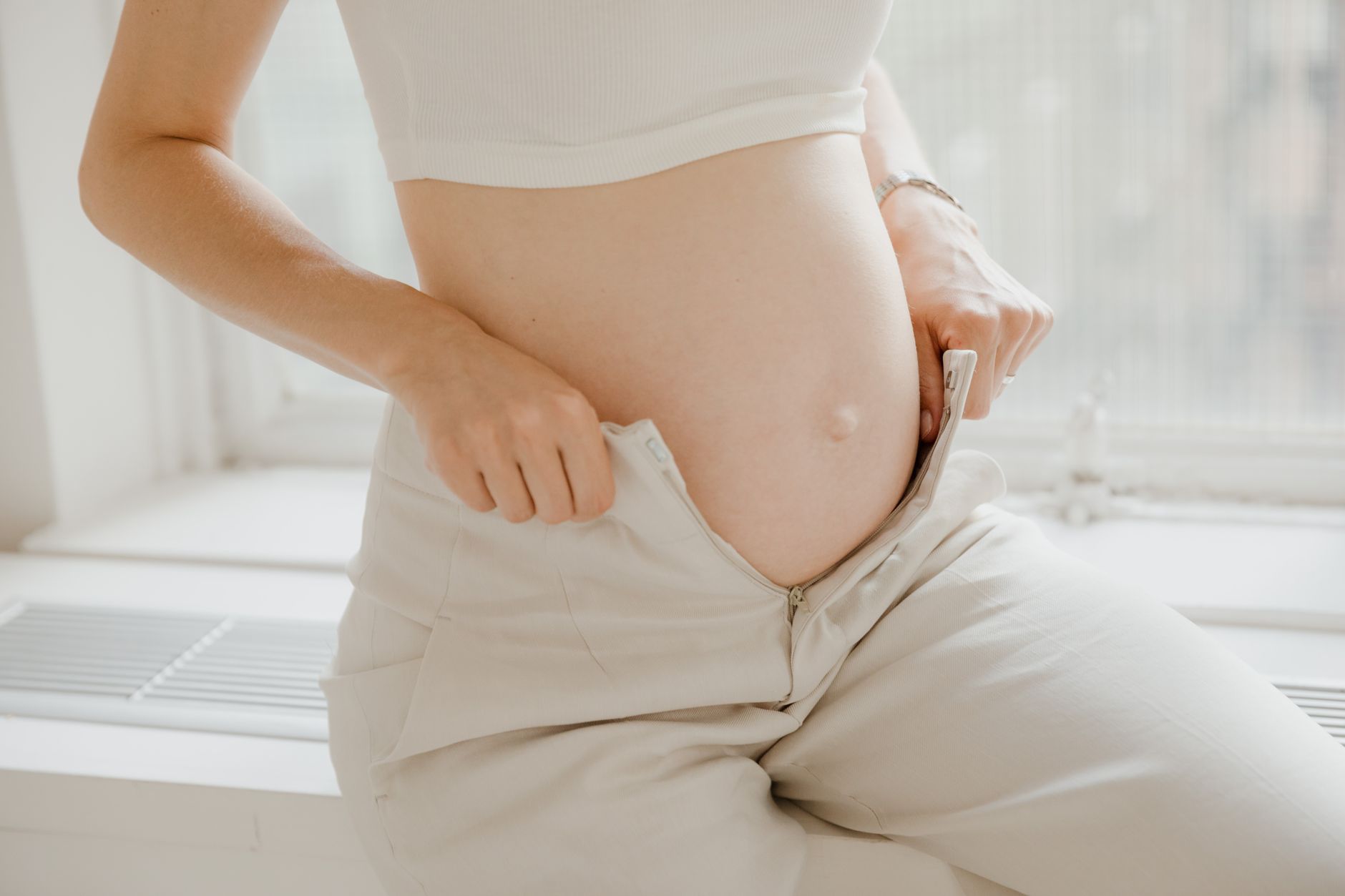 pregnant person applying a cold gel pack to their lower back while sitting on a couch