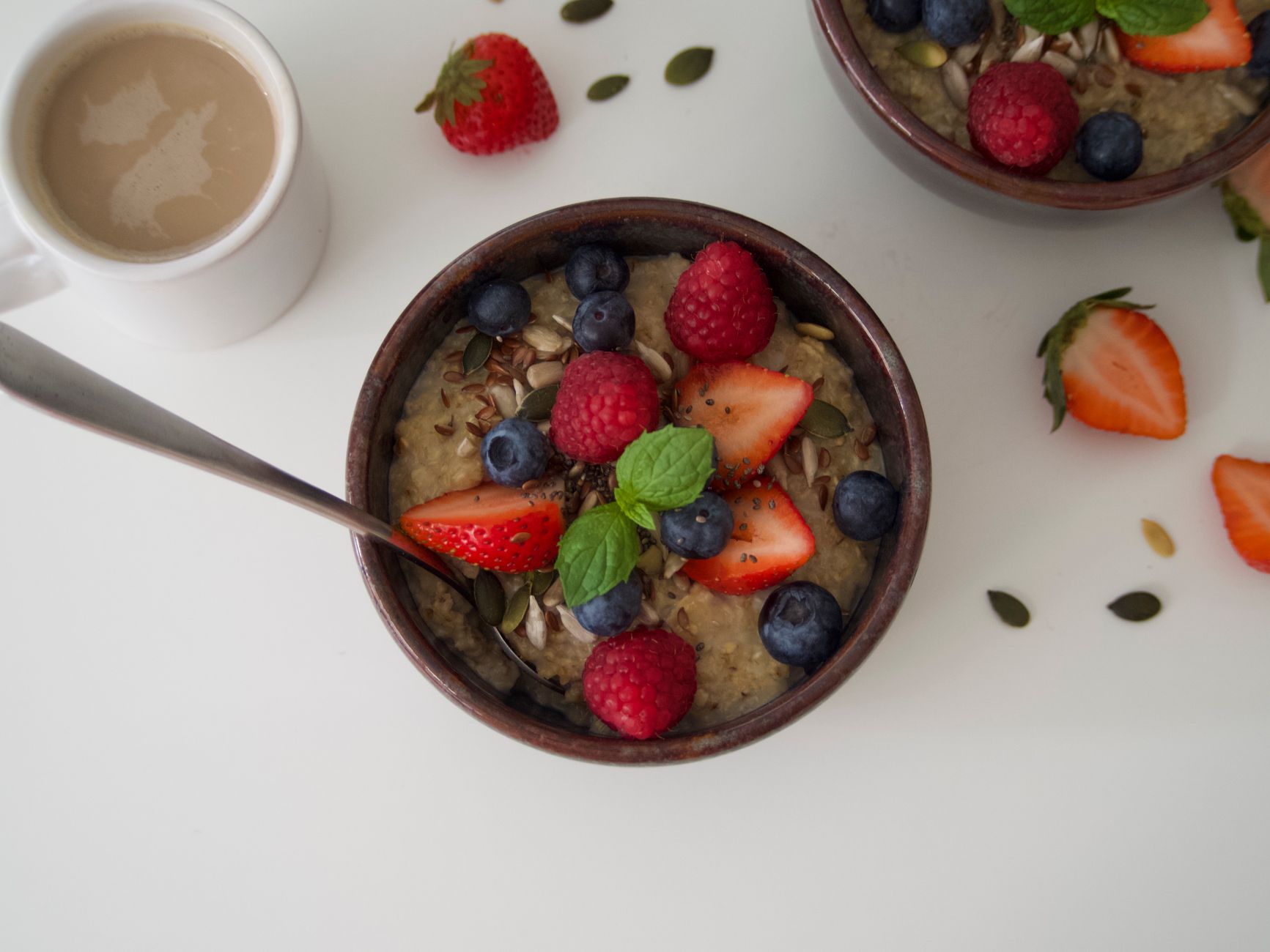 a neatly arranged breakfast table showing a bowl of oatmeal topped with almond milk, pumpkin seed powder, and fresh berries, with a steaming cup of ginger tea beside it