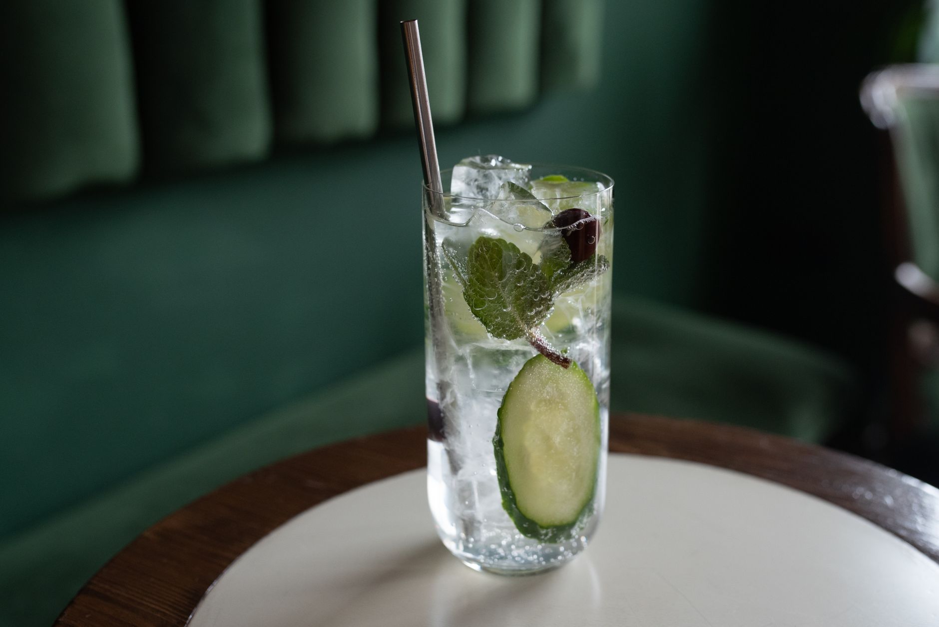 A collection of non‑alcoholic mocktail ingredients: a bottle of Seedlip Garden 108, fresh cucumber slices, lime wedges, and a sprig of mint arranged on a marble countertop