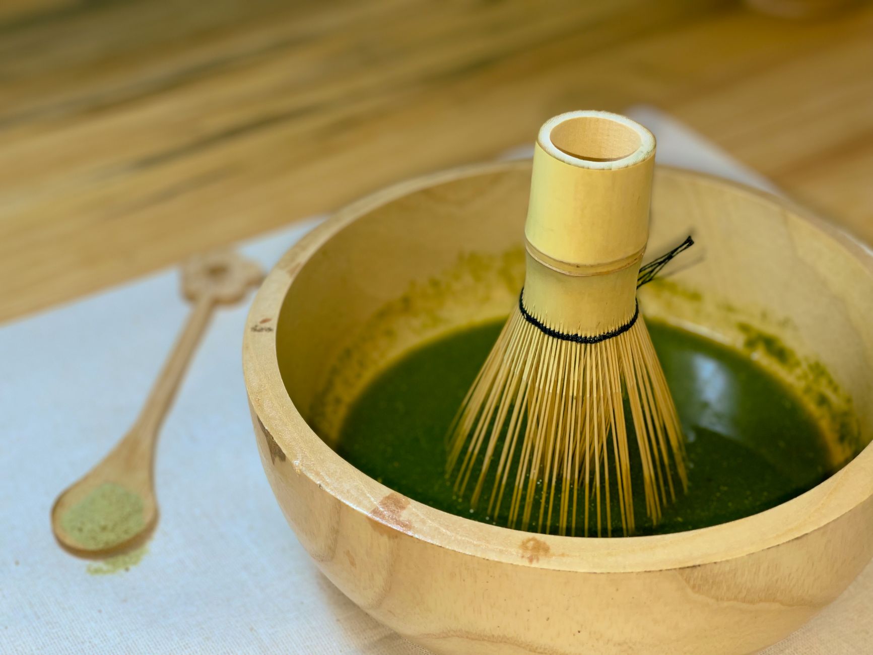 Close‑up of vibrant green matcha powder in a bamboo whisk bowl, bright natural light highlighting the fine texture