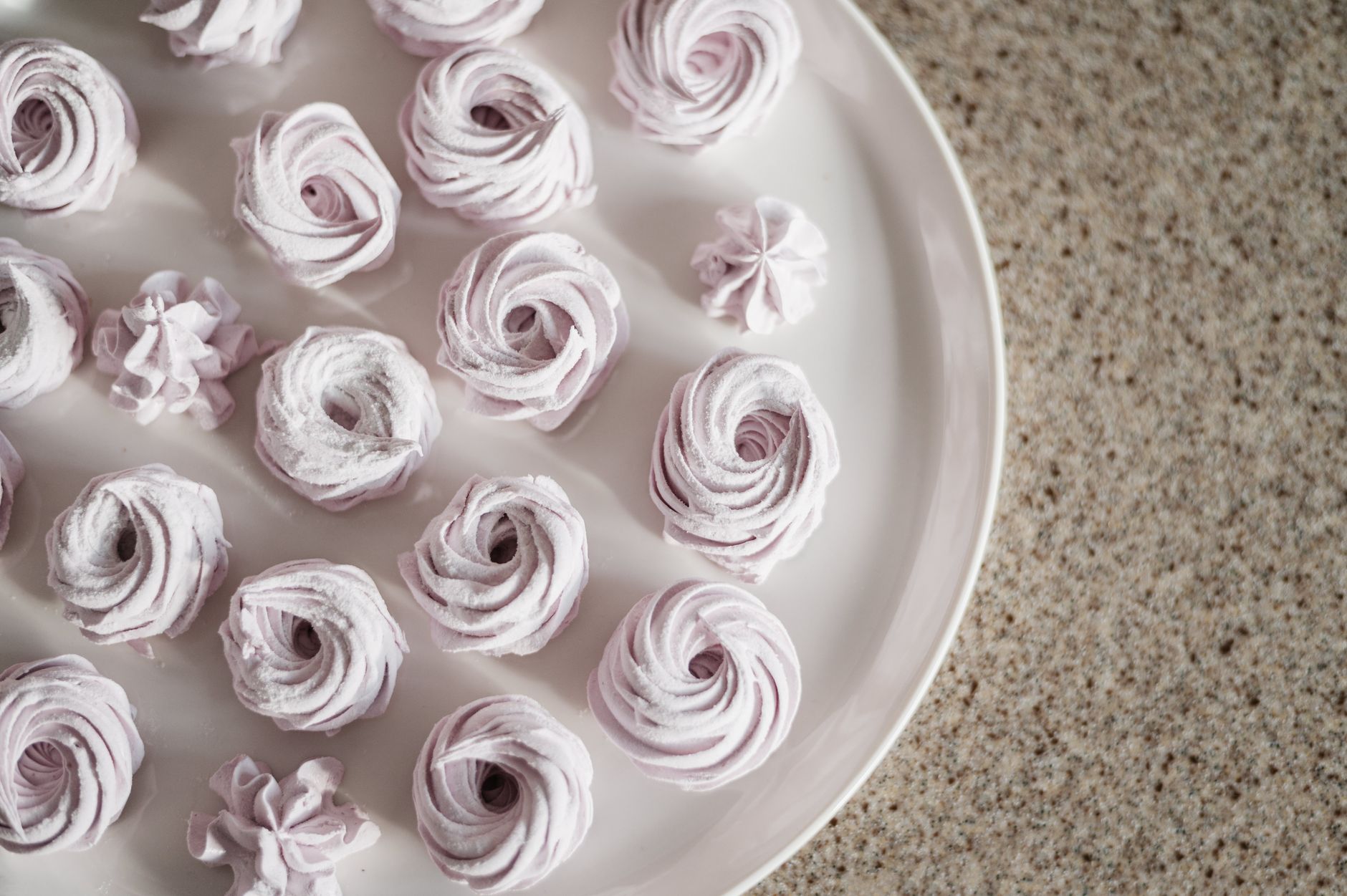 a tray of pastel-colored baked meringue cookies on a white plate, showing crisp edges and a lightly browned top, perfect for a pregnancy-friendly dessert