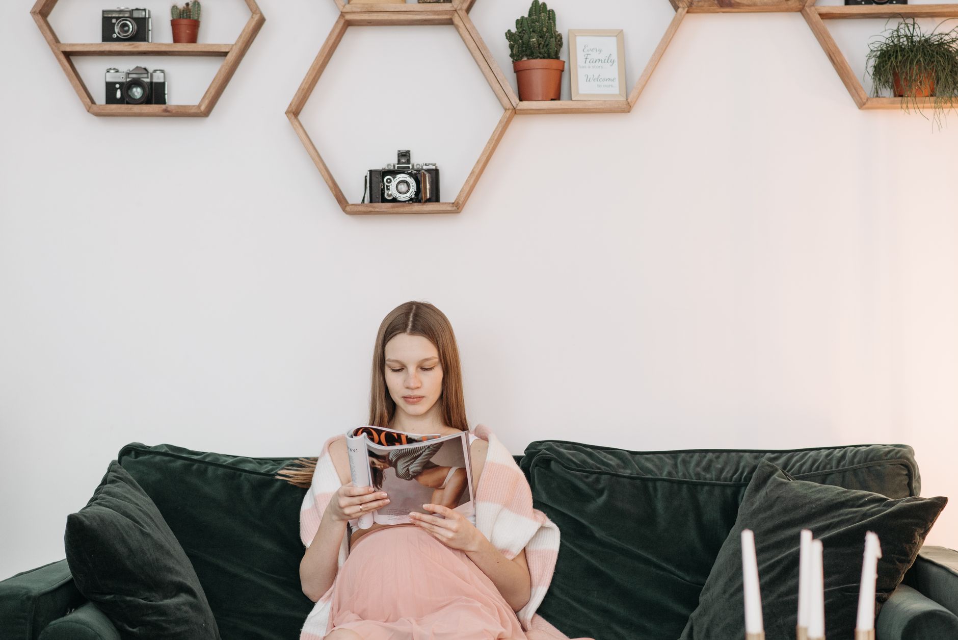 A thoughtful pregnant woman sitting on a couch, gently caressing her belly, with a medical pamphlet or book on a coffee table nearby. Soft, comforting home environment.