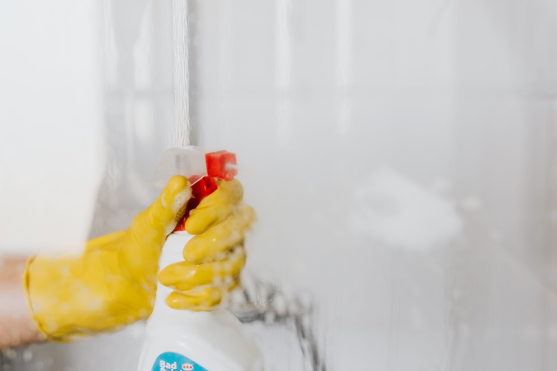 A pregnant woman wearing a mask and gloves, holding a spray bottle while standing in a well‑ventilated bathroom, highlighting safe cleaning practices.