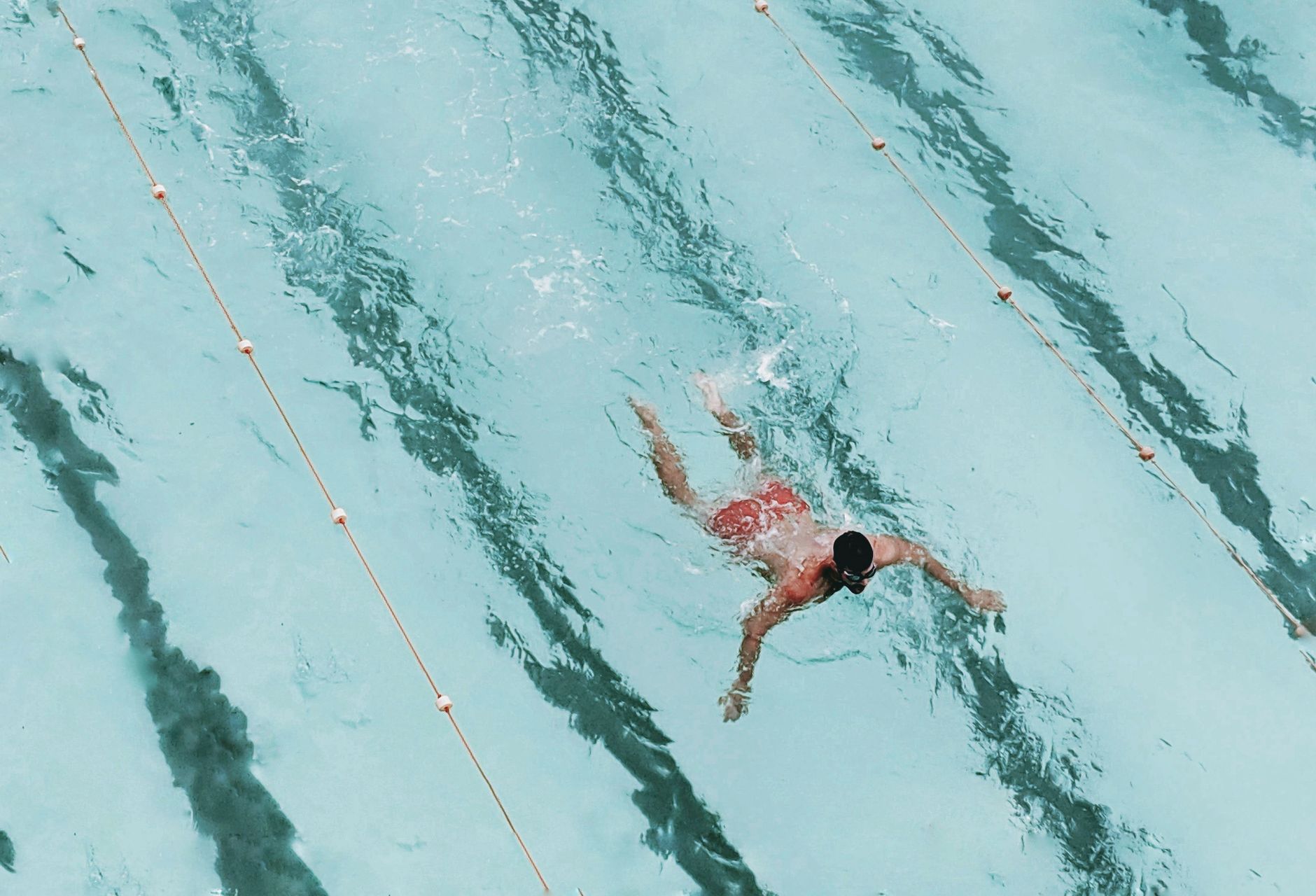 A serene image of a pregnant woman swimming laps in a clear blue pool, with sunlight reflecting off the water, emphasizing calm and gentle exercise.