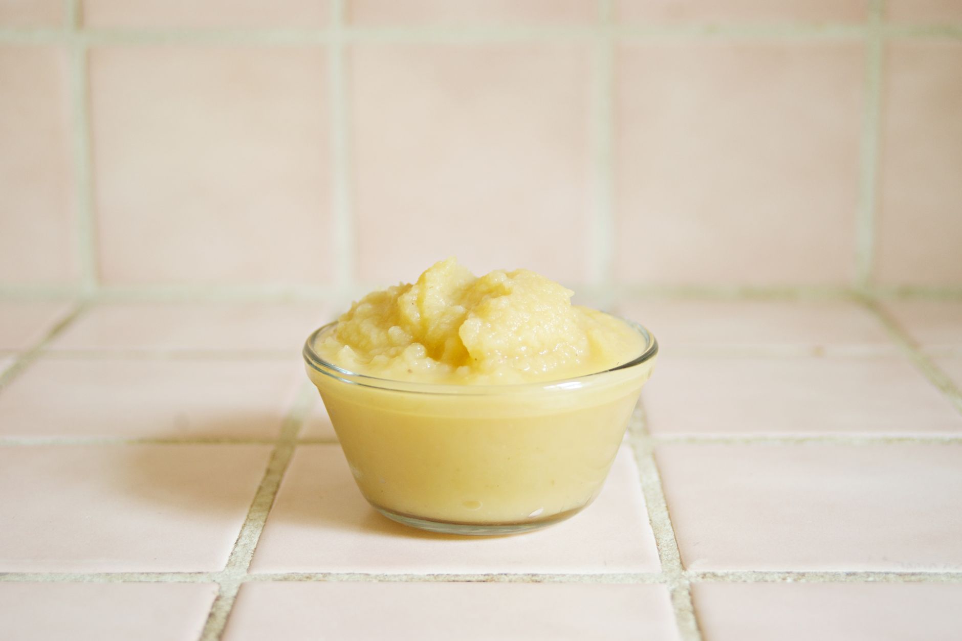 A colorful bowl of mashed avocado, sweet potato, and iron‑fortified cereal on a wooden plate, with a small spoon beside it