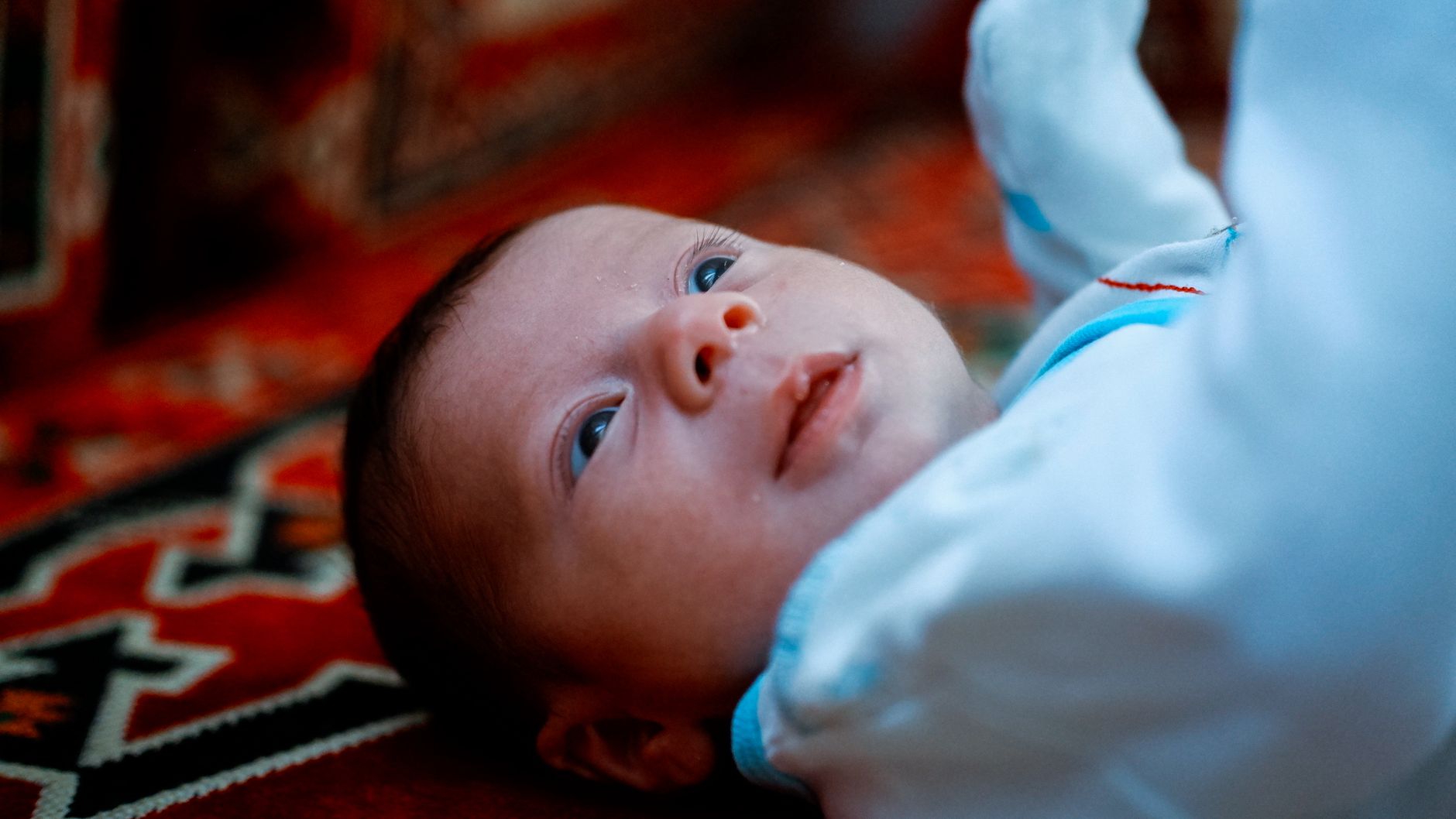 A parent gently rocking a baby in a dimly lit nursery, with a soft blanket draped over them