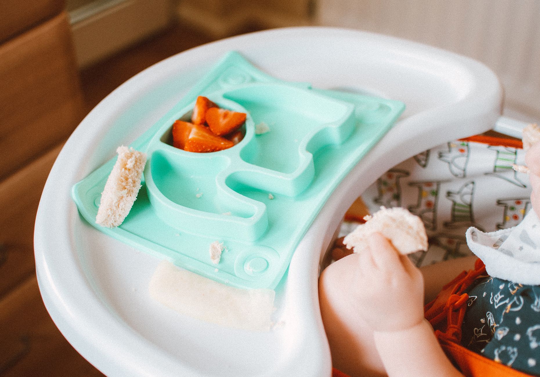 A close-up of a baby's hands exploring a soft, cooked carrot stick on a high chair tray, showing good hand-eye coordination